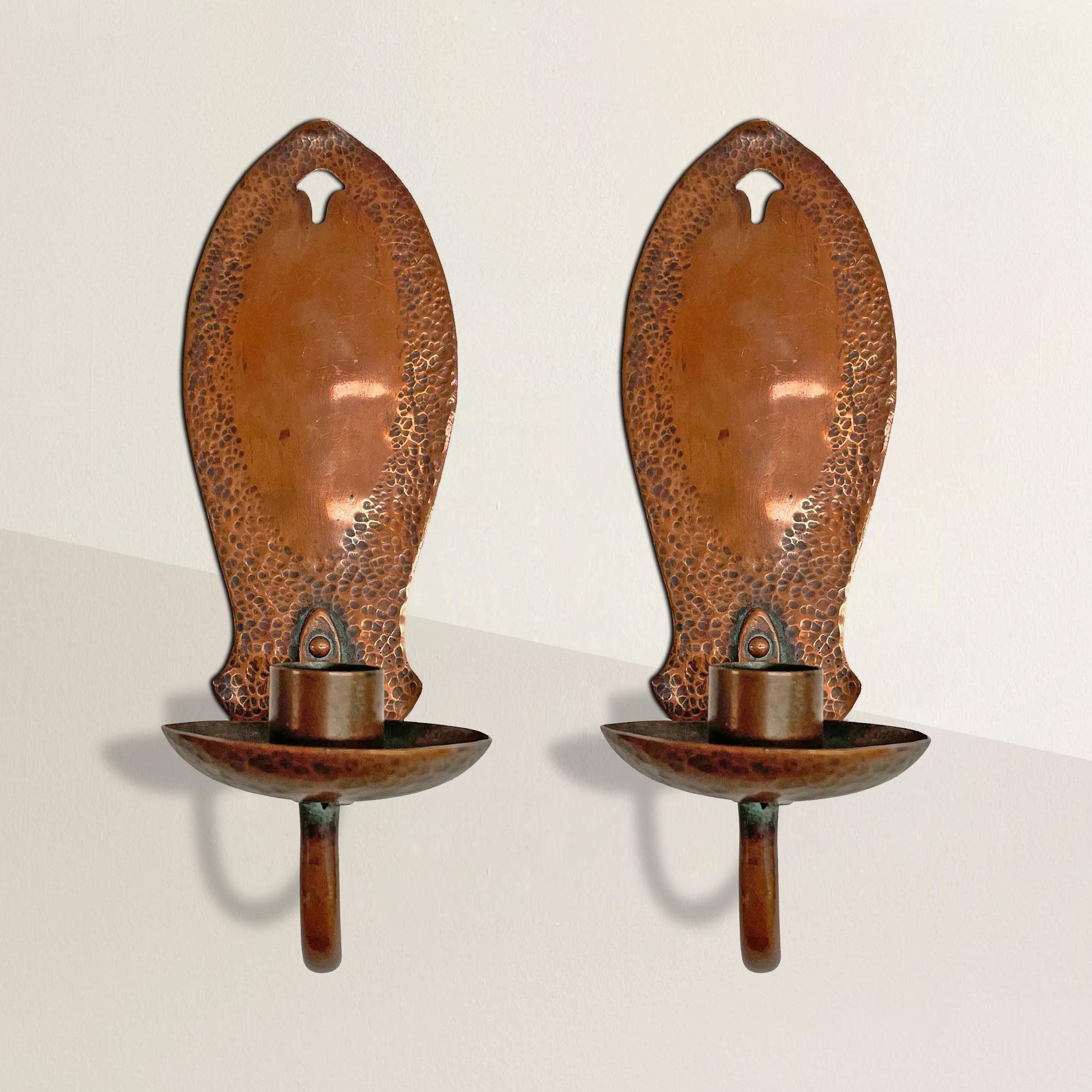 A handsome pair of late 19th century English Arts & Crafts copper candle sconces with hand-hammered backplates, a hammered candle cup attached to a simple curved arm with a sweet floral rivet, and one of the best patinas we've seen in a long time.