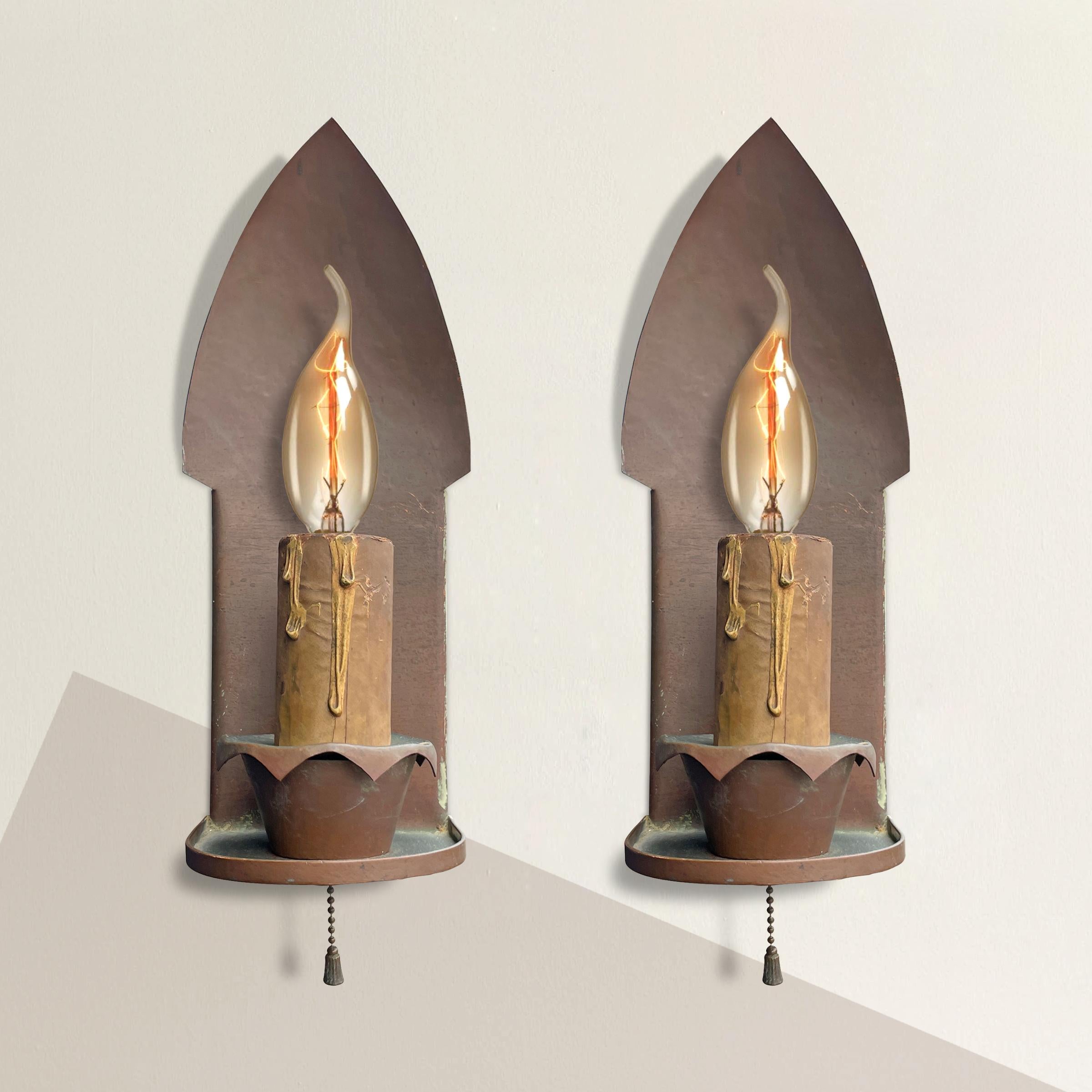 A charming pair of English Arts & Crafts hammered copper sconces, each with protruding arched backplates, faux candles, scalloped candle cups, and pulls chains.