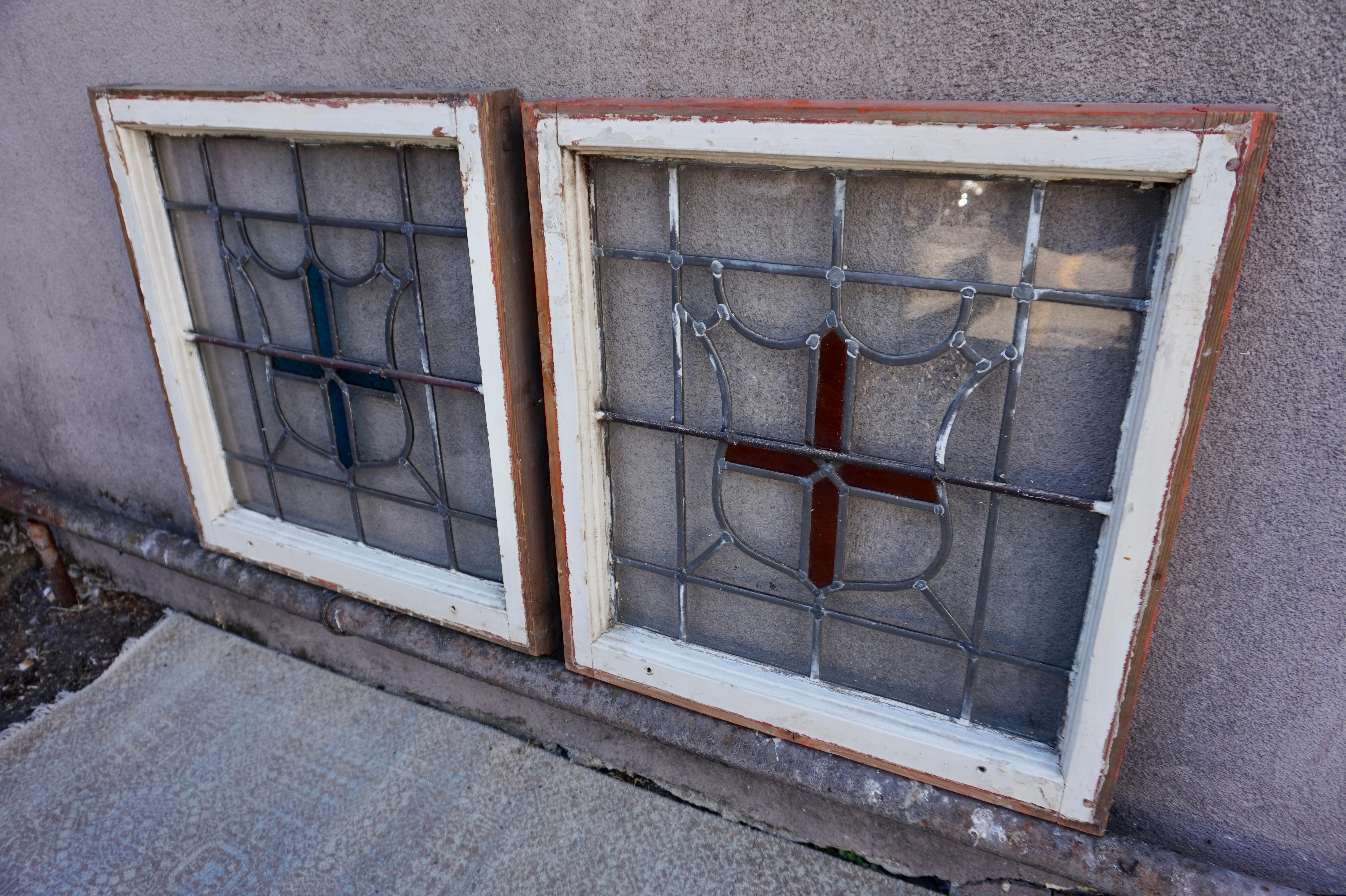 Seltenes Arts & Crafts-Paar von Glasfenstern mit Schildmotiv. Schön konstruiert und in gutem Originalzustand, ohne Holzfäule. Diese haben auf einer Seite Gitterstäbe. Ein Schild hat ein türkisfarbenes Kreuz, der andere ein bernsteinfarbenes. Sehr
