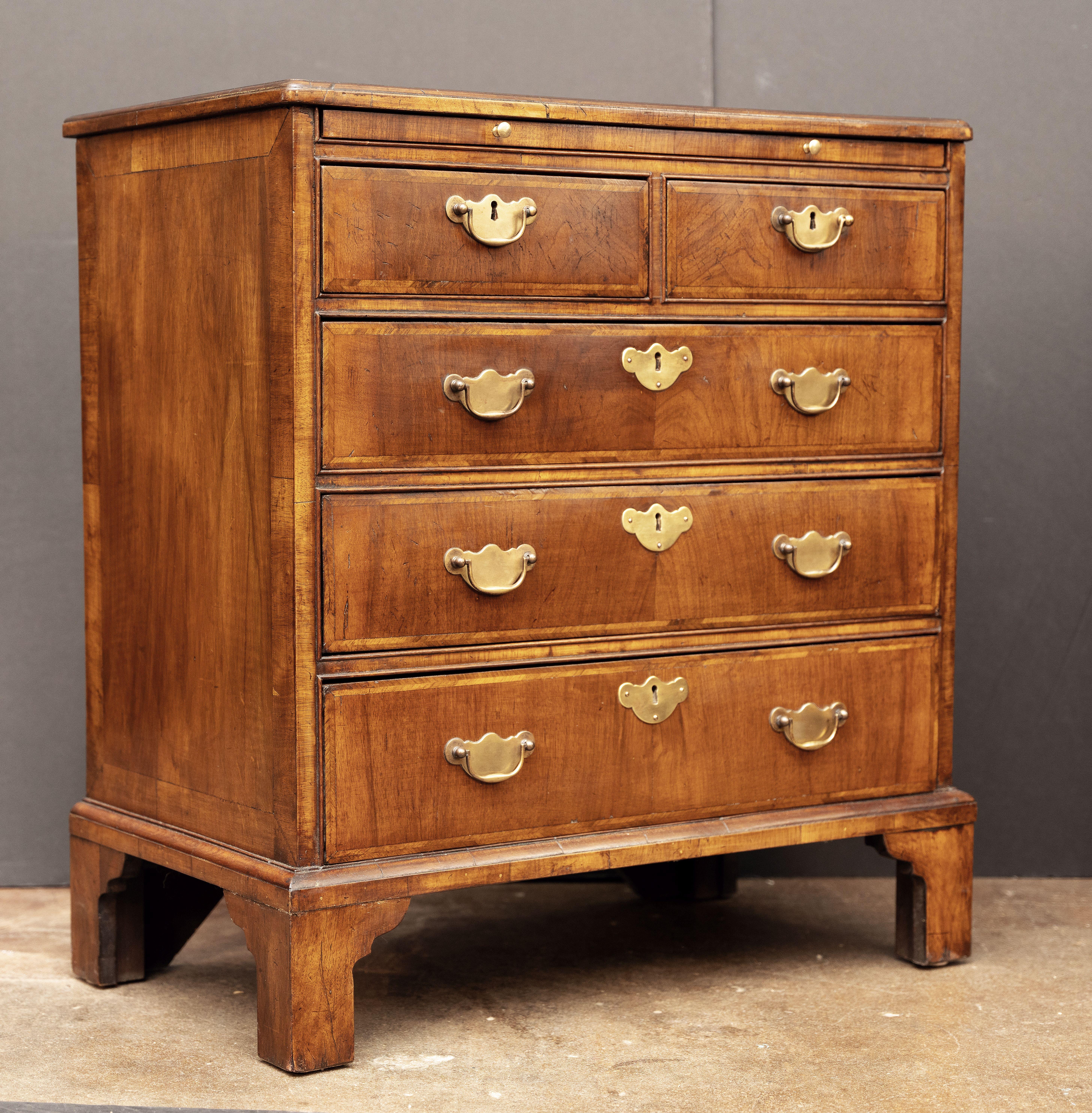 A fine pair of period English small or short bachelor's chest of drawers (or side chests) of walnut with feather banding, c.1820, from the late Georgian Era, each chest featuring a mahogany moulded top over a bachelor's slide and three drawers, all
