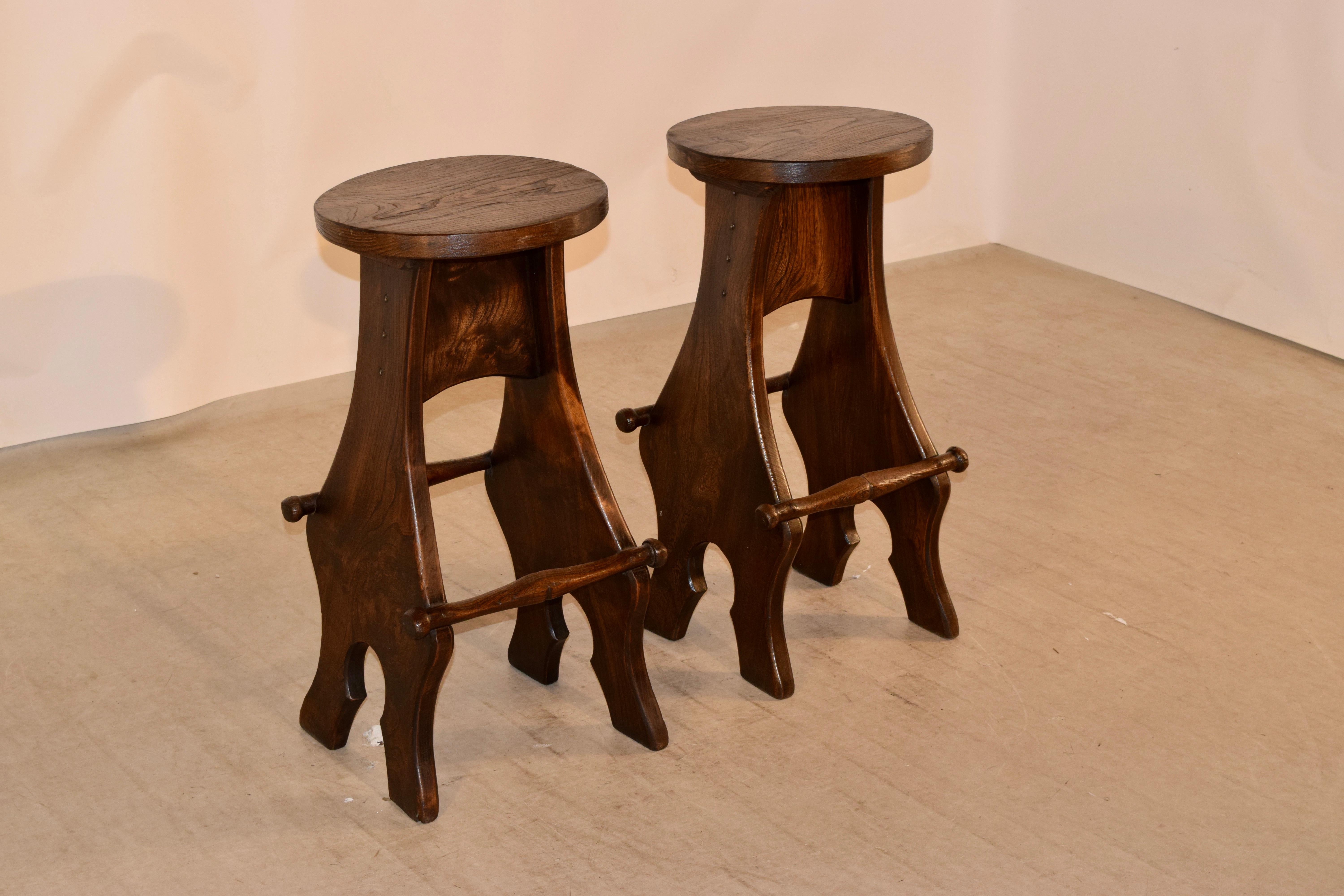 Pair of English barstools made of elm. The seats are wonderfully grained and are supported on trestle type sides which end in shaped feet. The sides are joined by hand-turned stretchers, also used for resting your feet. Great shape and design.