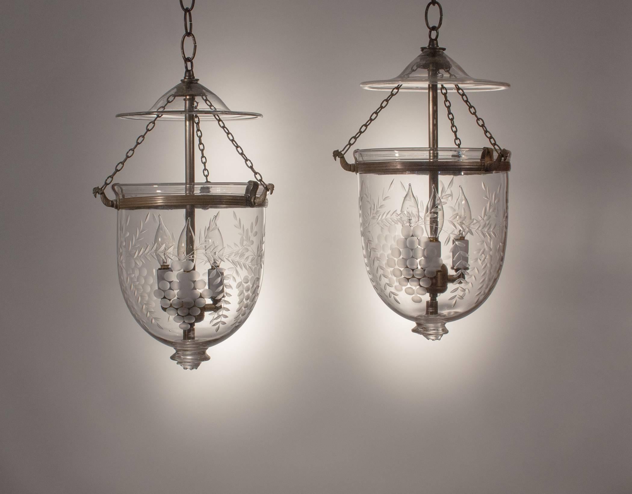 A lovely, well-matched pair of antique bell jar lanterns from England. These circa 1870 pendants boast excellent quality handblown glass and a finely etched vine with grape design that suits the contours of the hall lanterns nicely. The rolled brass