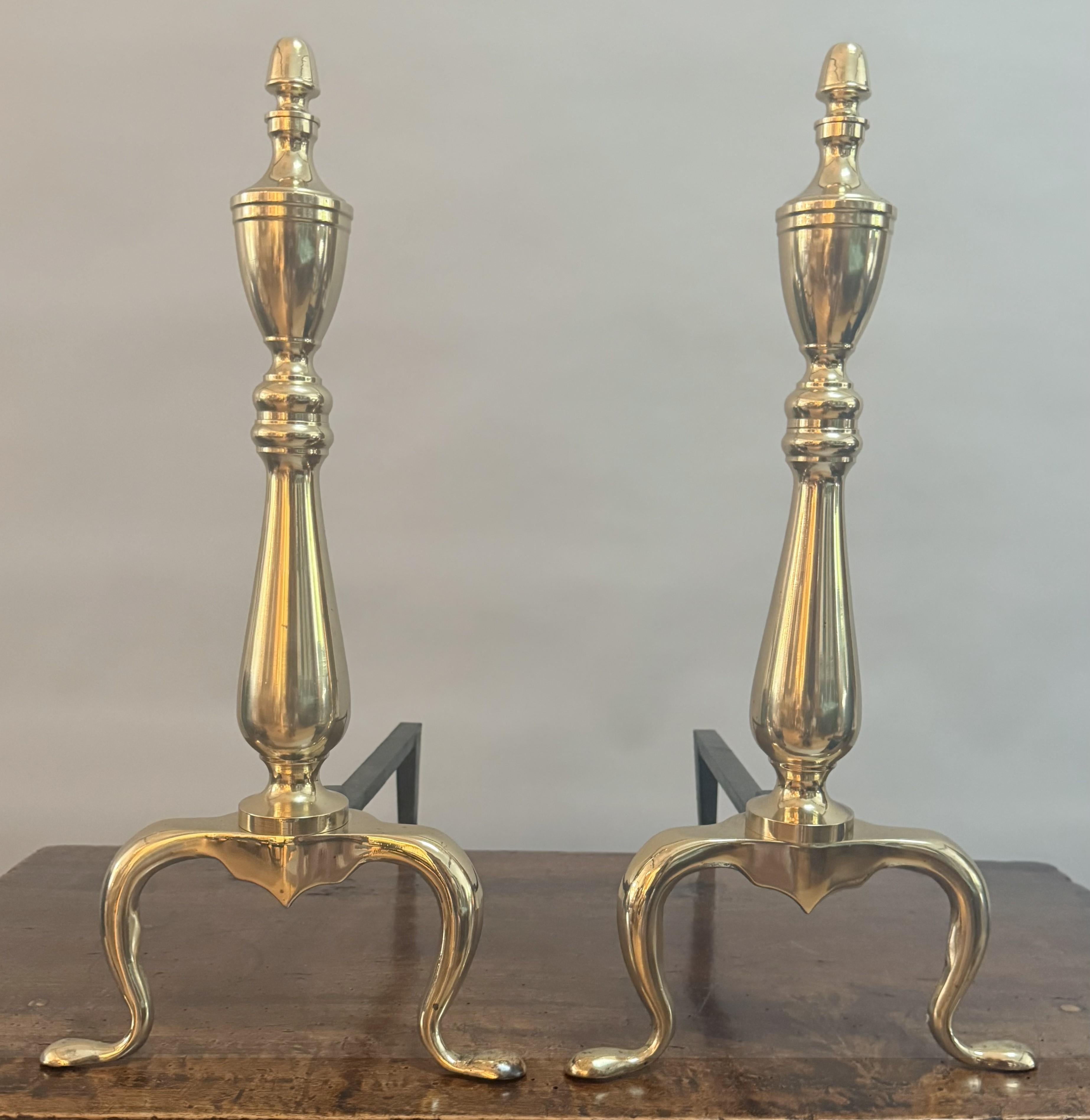 A refined pair of mid-19th-century English brass andirons, radiating timeless Georgian elegance! Each standard rises in a finely turned baluster form, crowned with a classical urn-form finial, a motif long celebrated for its symbolism of refinement