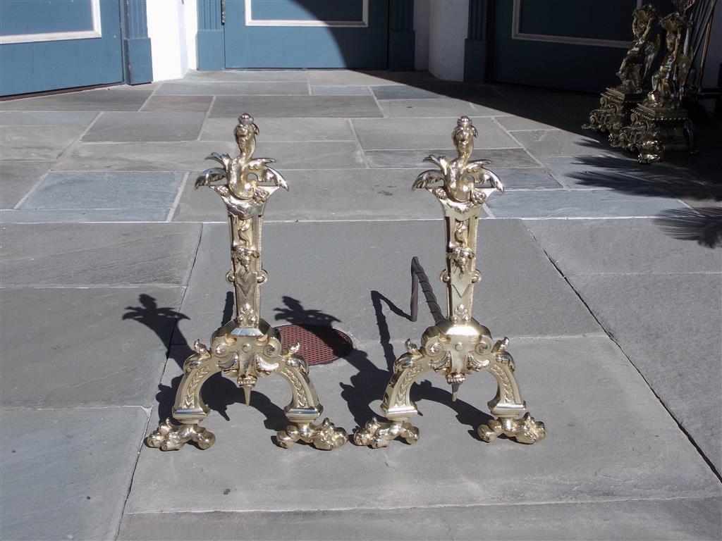 Pair of English brass flanking dragon finial andirons with decorative foliage plinths, original rear wrought iron spiral dog legs, and resting on scrolled foliage legs with lions paw feet. Mid 19th Century.