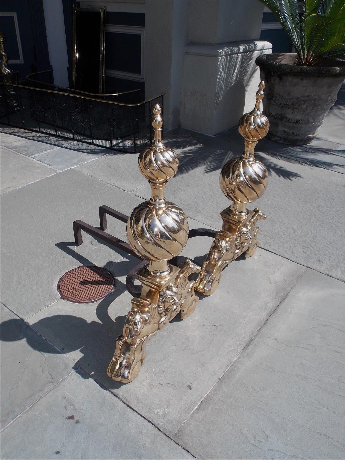 Pair of English brass spiral ball on ball andirons with bulbous urn finials, squared plinths with centered mask lions, matching brass ball log stops with original wrought iron dog legs, and resting on flanking Pegasus with claw and ball feet,