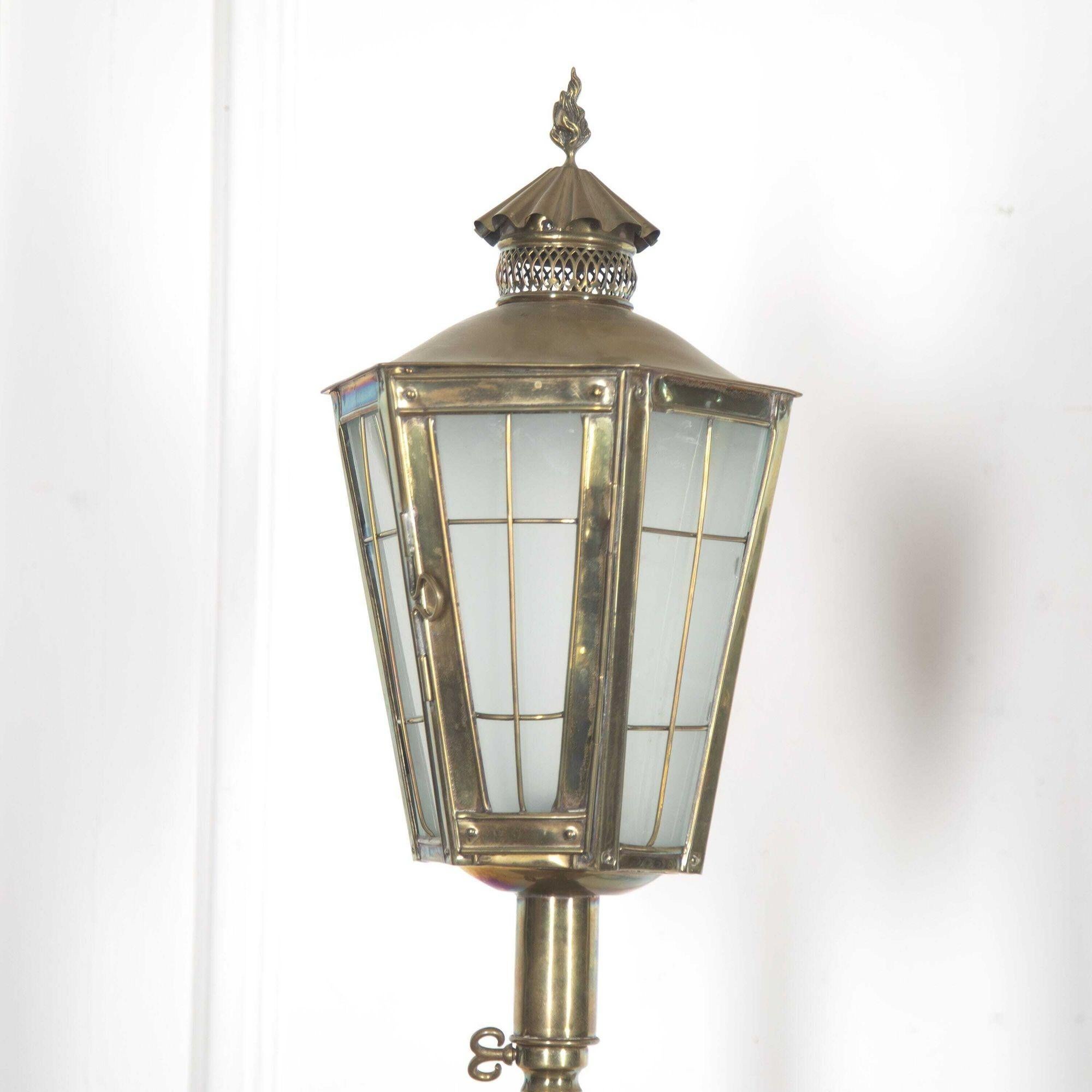 Wonderful pair of English brass standing lanterns, circa 1920. 
These lanterns have a tapered glazed body with an opening door and a finely pierced chimney. These chimneys are topped with a cast brass flame.
The glass panels are smoked so that
