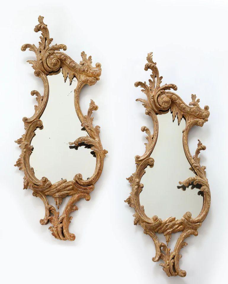 A fine pair of English, carved rococo cartouche shaped looking glasses circa 1755 designed of c-scrolls and s-scrolls, crested with an acanthus spray, one scroll carved with egg and dart having acanthus sprays and rocaille, the frame with numerous