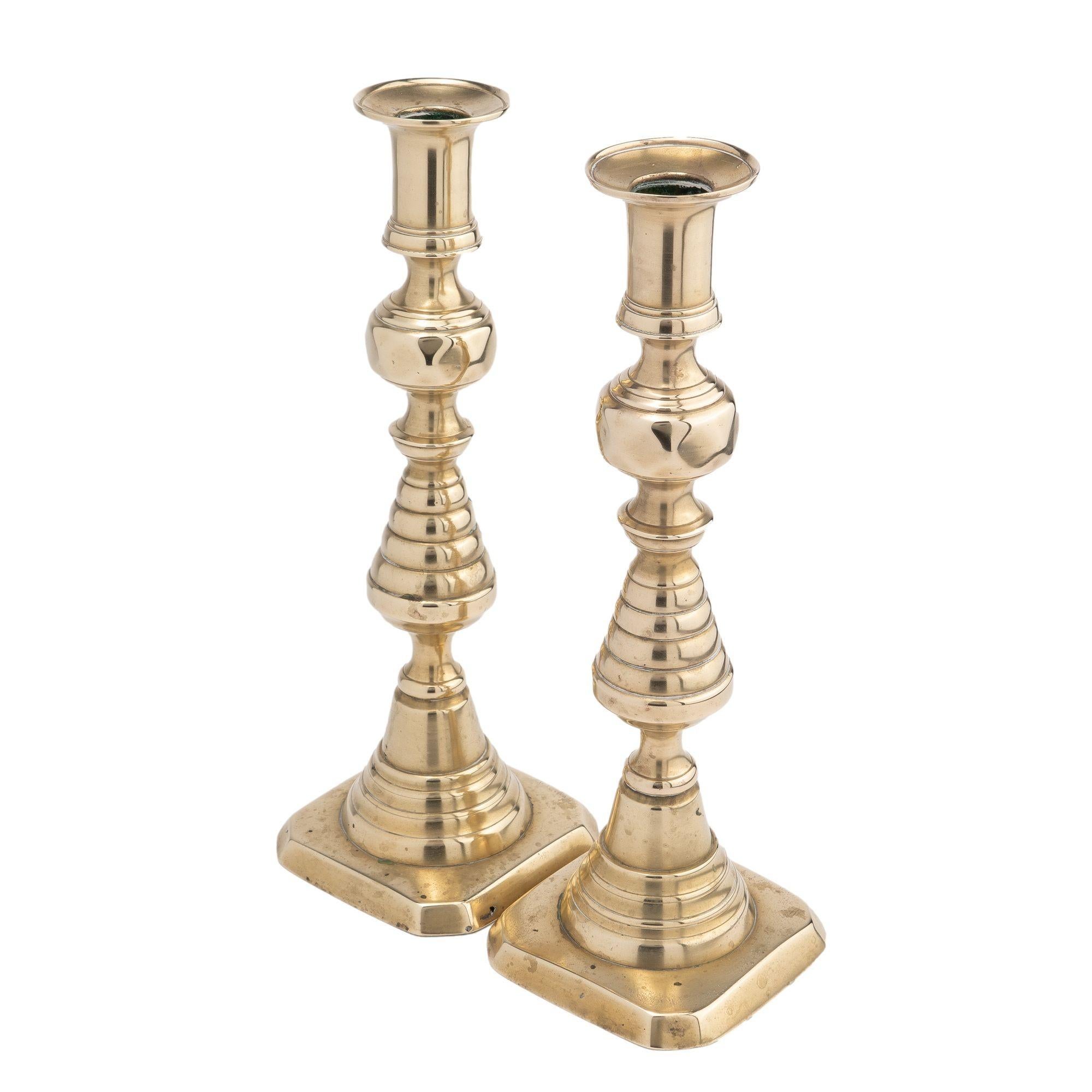 Pair of hollow core cast brass beehive candlesticks with classic urn form candle cut with bobeshe. Below the bobeshe is a diamond facetted knob on a beehive turning, peened to a conical stepped dome on a raised square base with cut corners. Both