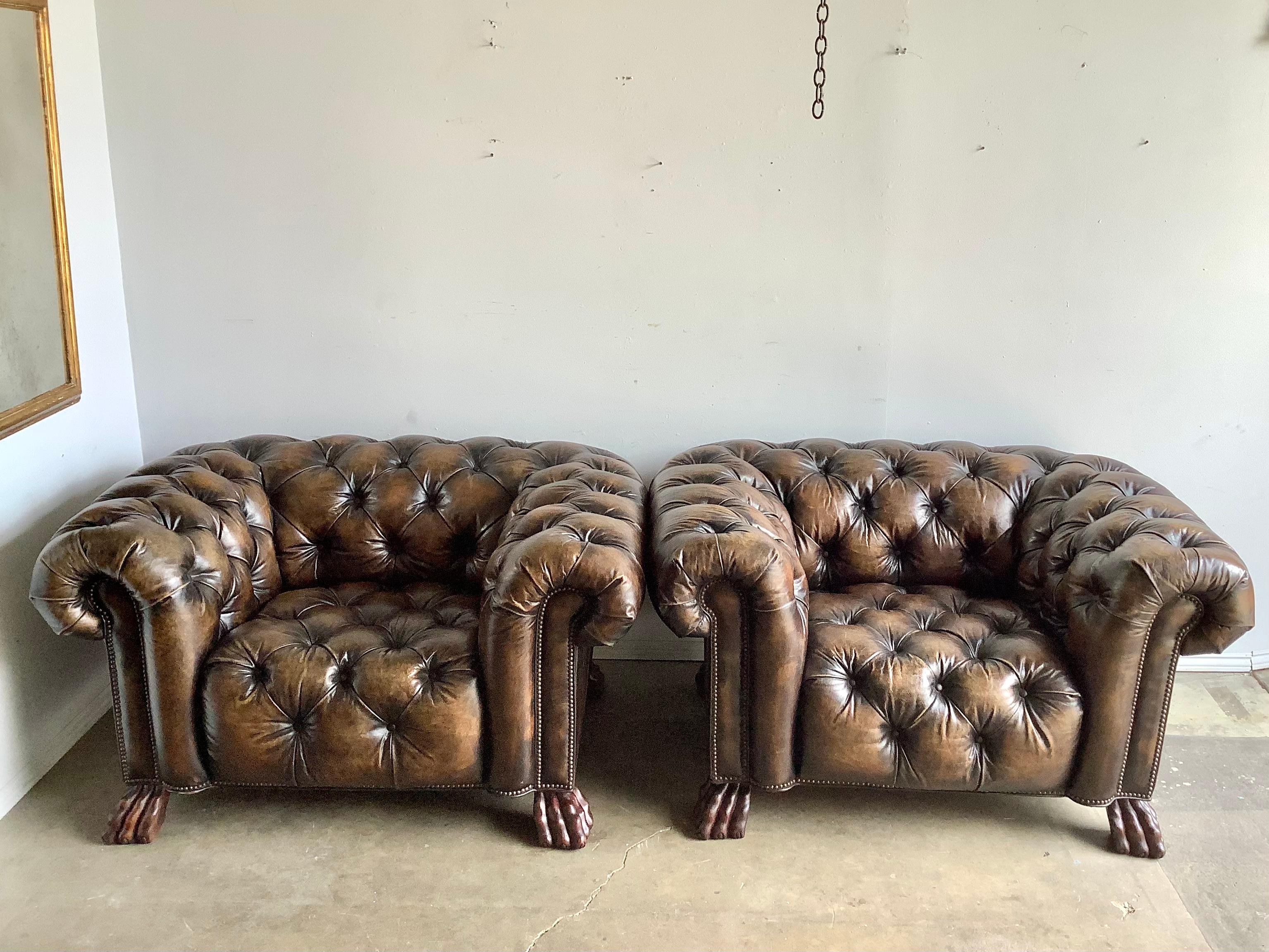 Pair of English leather tufted Chesterfield style armchairs standing on carved wood Lion Paw Feet. The chairs are upholstered in a beautiful tobacco color that has worn well throughout the years. Great overall condition.