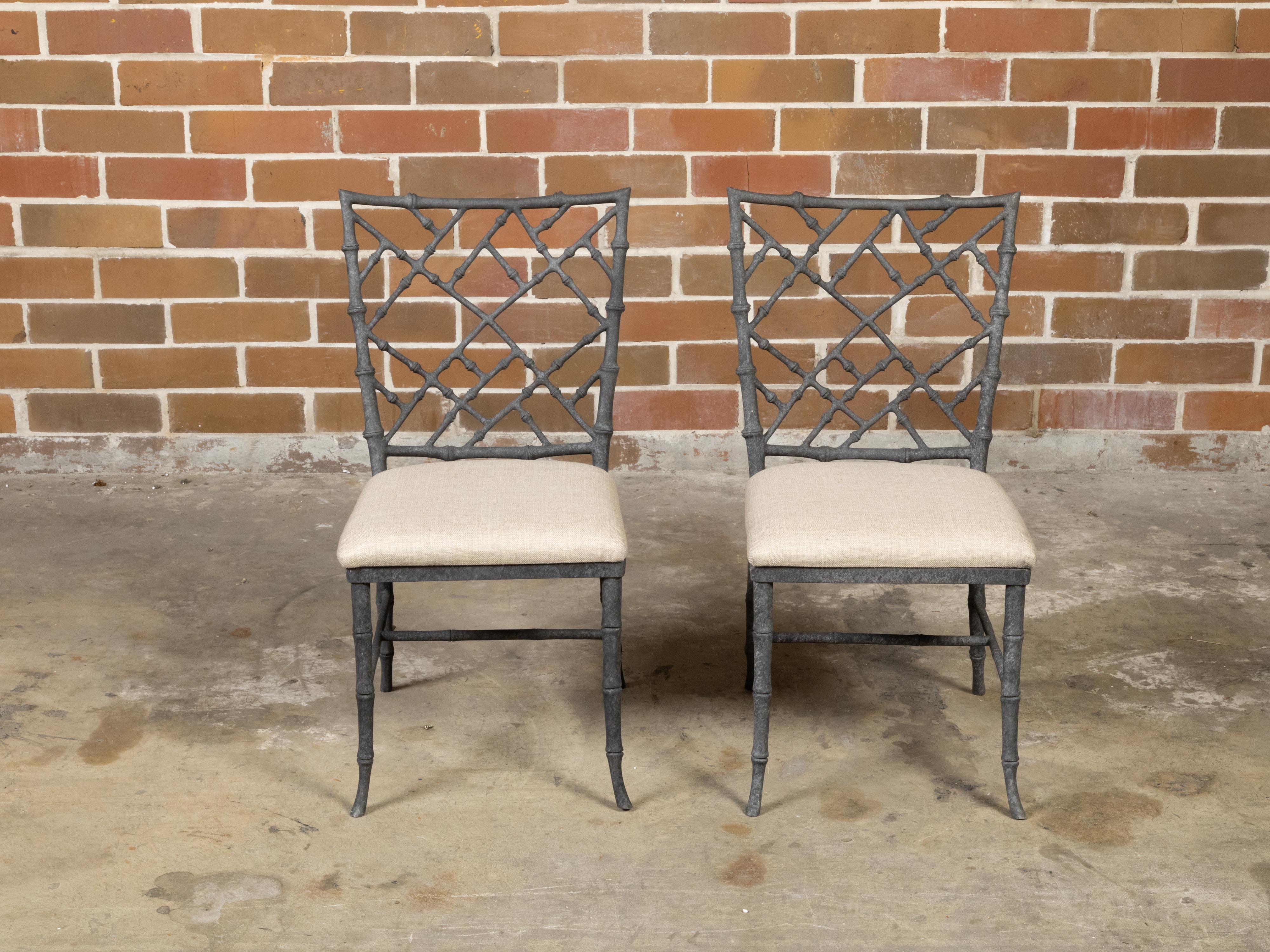 A pair of English Chinese Chippendale style iron side chairs from the mid 20th century with intricate backs, grey color, faux bamboo structure and new linen upholstery. Created in England during the Midcentury period, each of this pair of side