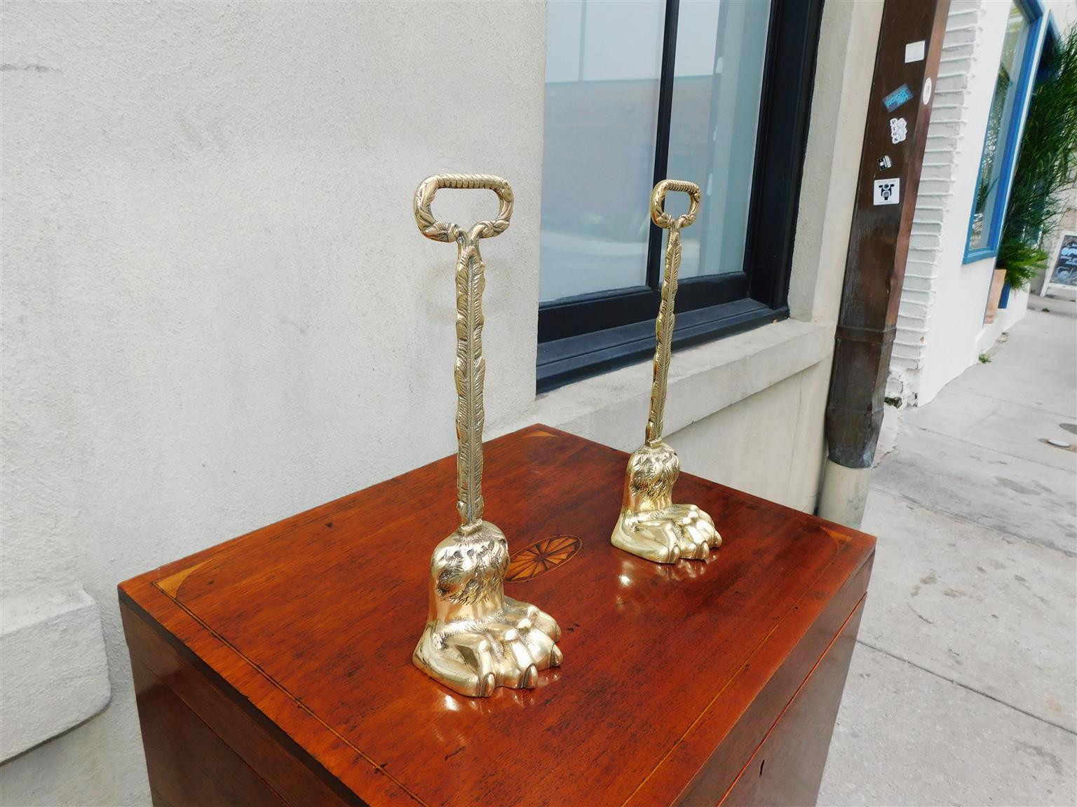 Pair of English Chippendale brass lion paw door stops with gadrooned foliage oval handles, feather banding columns, original interior lead inserts, and resting on hairy paw lion feet. Late 18th Century