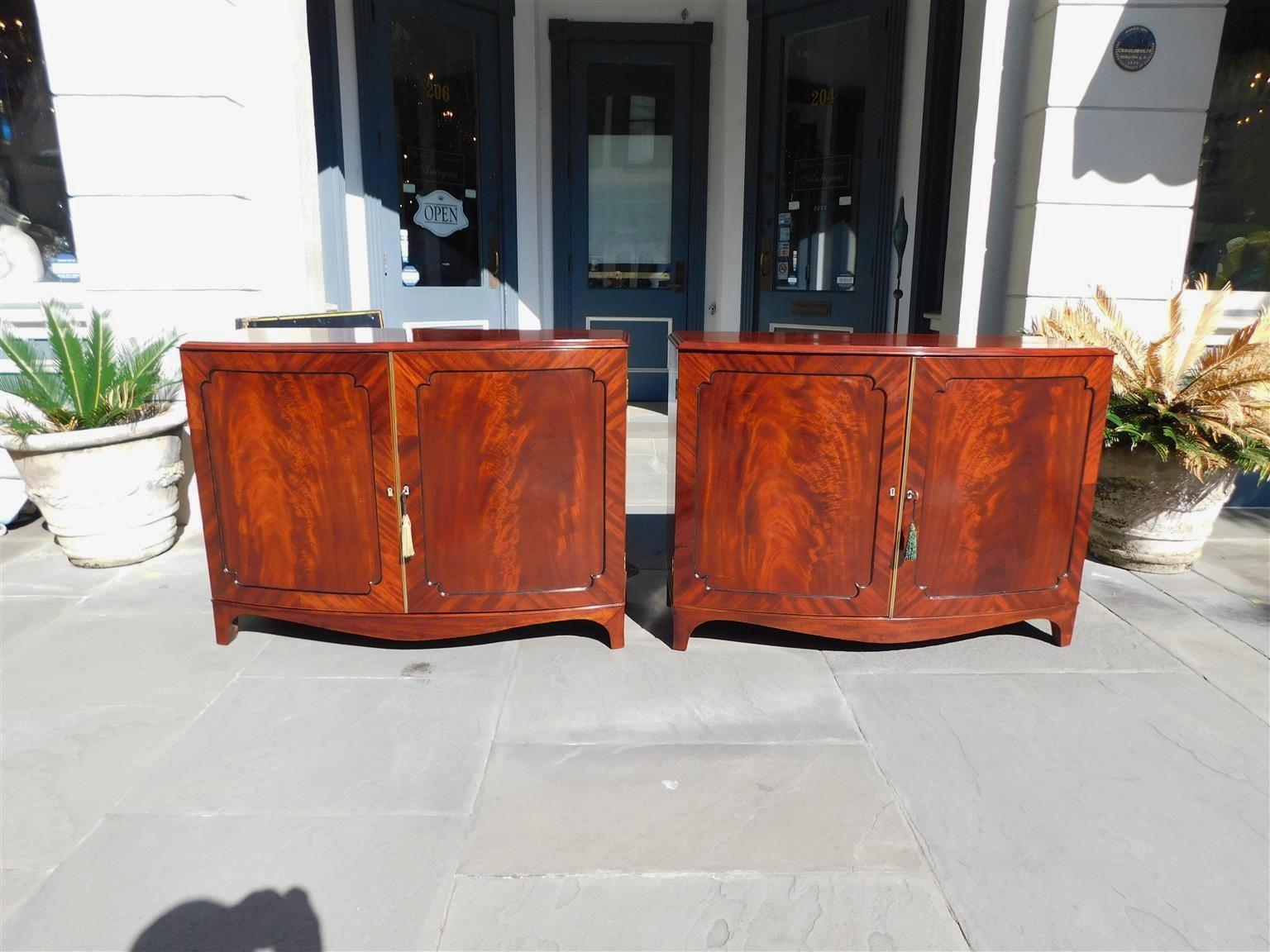 Pair of English Chippendale mahogany bow-front credenzas with carved molded edge tops, flanking book matched crotch mahogany hinged doors, ebonized string inlays, carved bone diamond escutcheons, original locking mechanisms with keys, fitted
