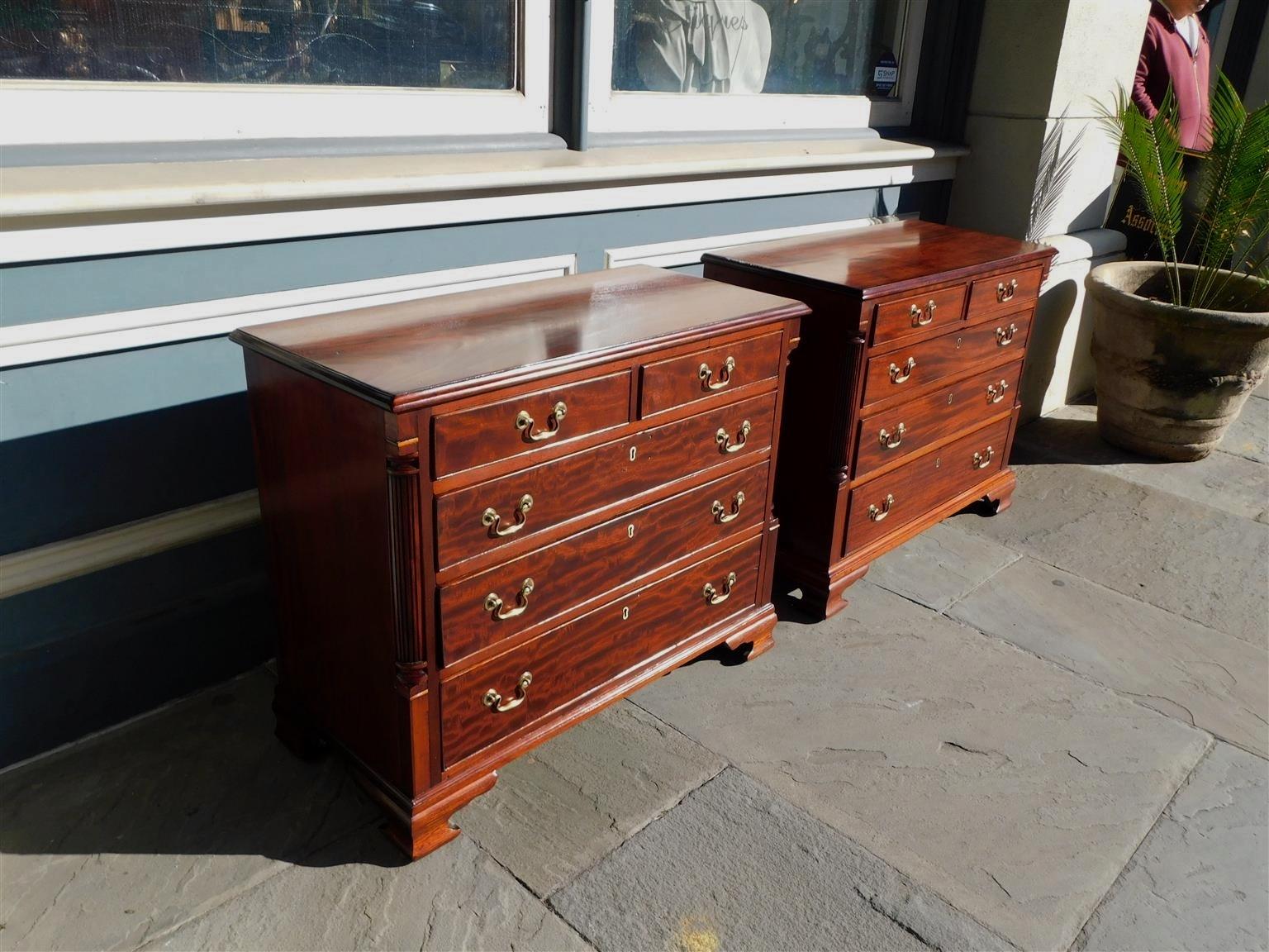 Pair of English Chippendale mahogany chest of drawers with carved molded edge tops, flanking reeded quarter columns, five graduated drawers with the original brasses, and resting on the original ogee bracket feet. Late 18th century.