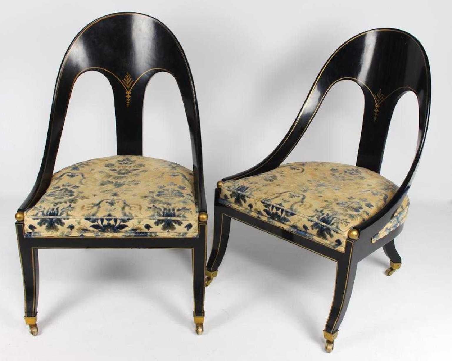 Pair of English Regency Revival spoon back slipper chairs in original high-polished black ground, hand decorated with gilt detailing and ball finials, klismos legs on solid brass casters. Seat cushions still have their original upholstery, an