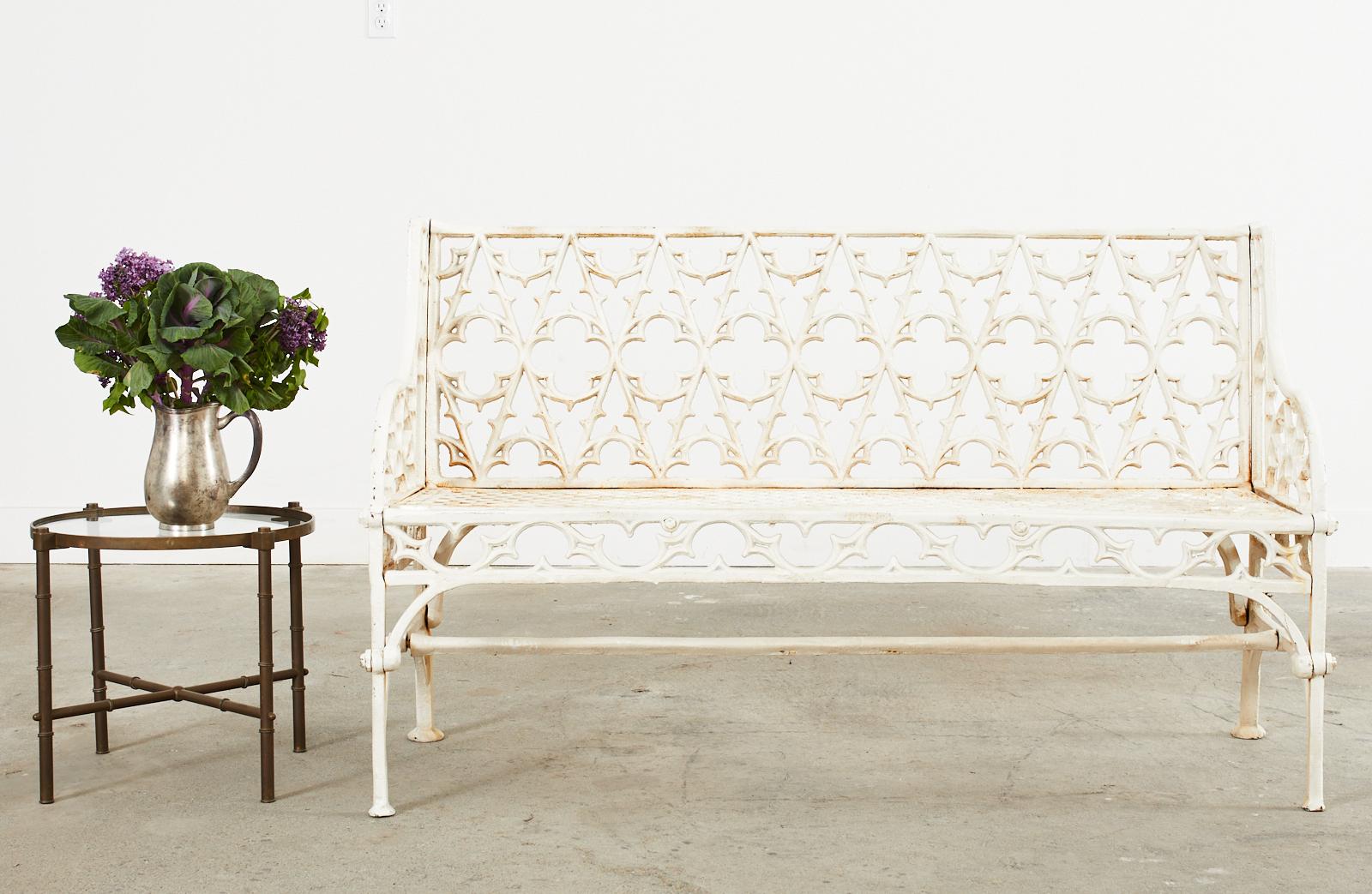 Stunning pair of white English Coalbrookdale foundry attributed cast iron garden benches. Made in the dramatic gothic revival taste featuring a gothic tracery backrest centered by quatrefoil form designs. The gracefully curved arms enclosing