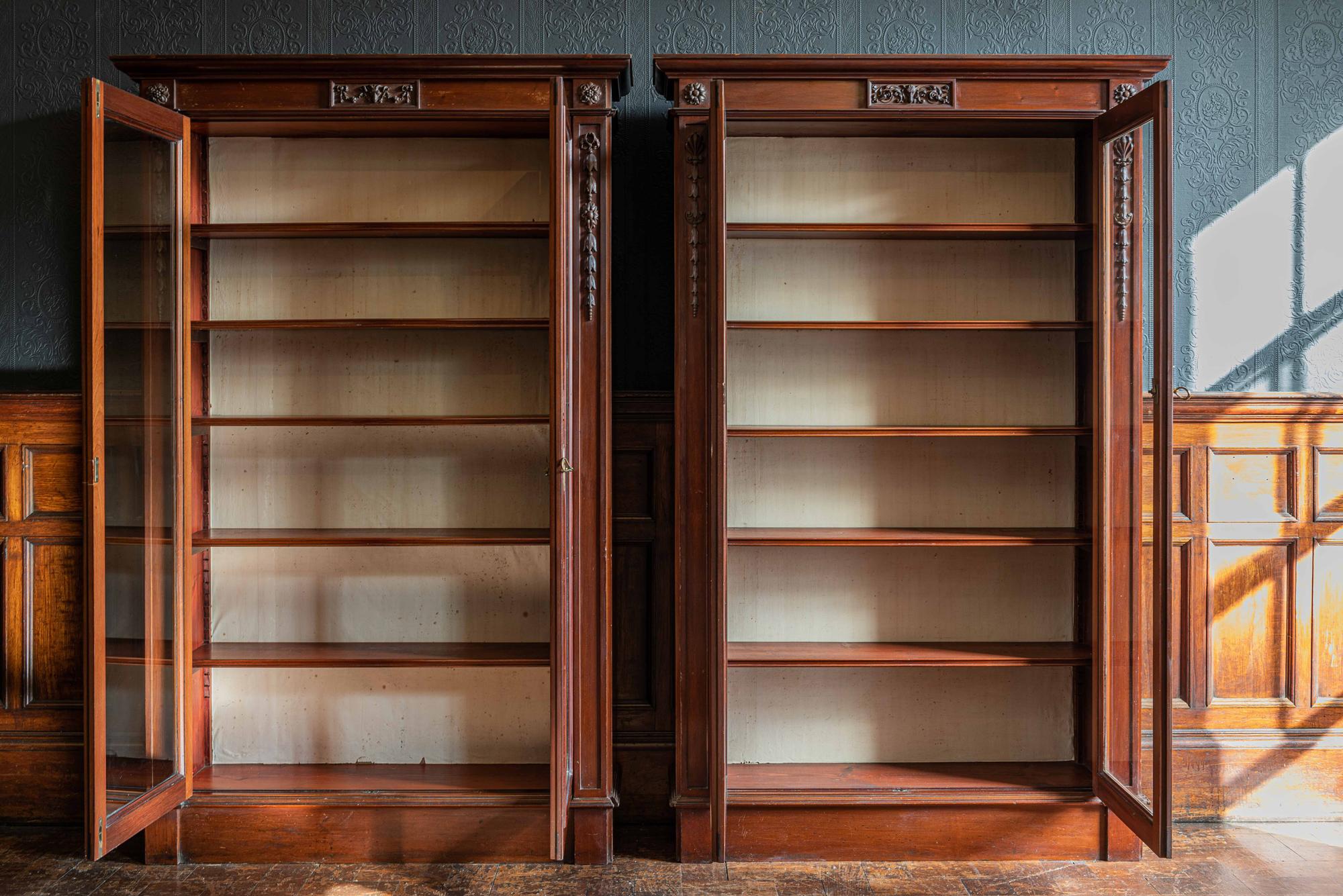 Pair of English country house solid mahogany glazed bookcases,
circa 1900.

A near pair of country house mahogany glazed bookcases, with adjustable shelves, the moulded cornice over a frieze, decorated to the center with a ram's head amongst