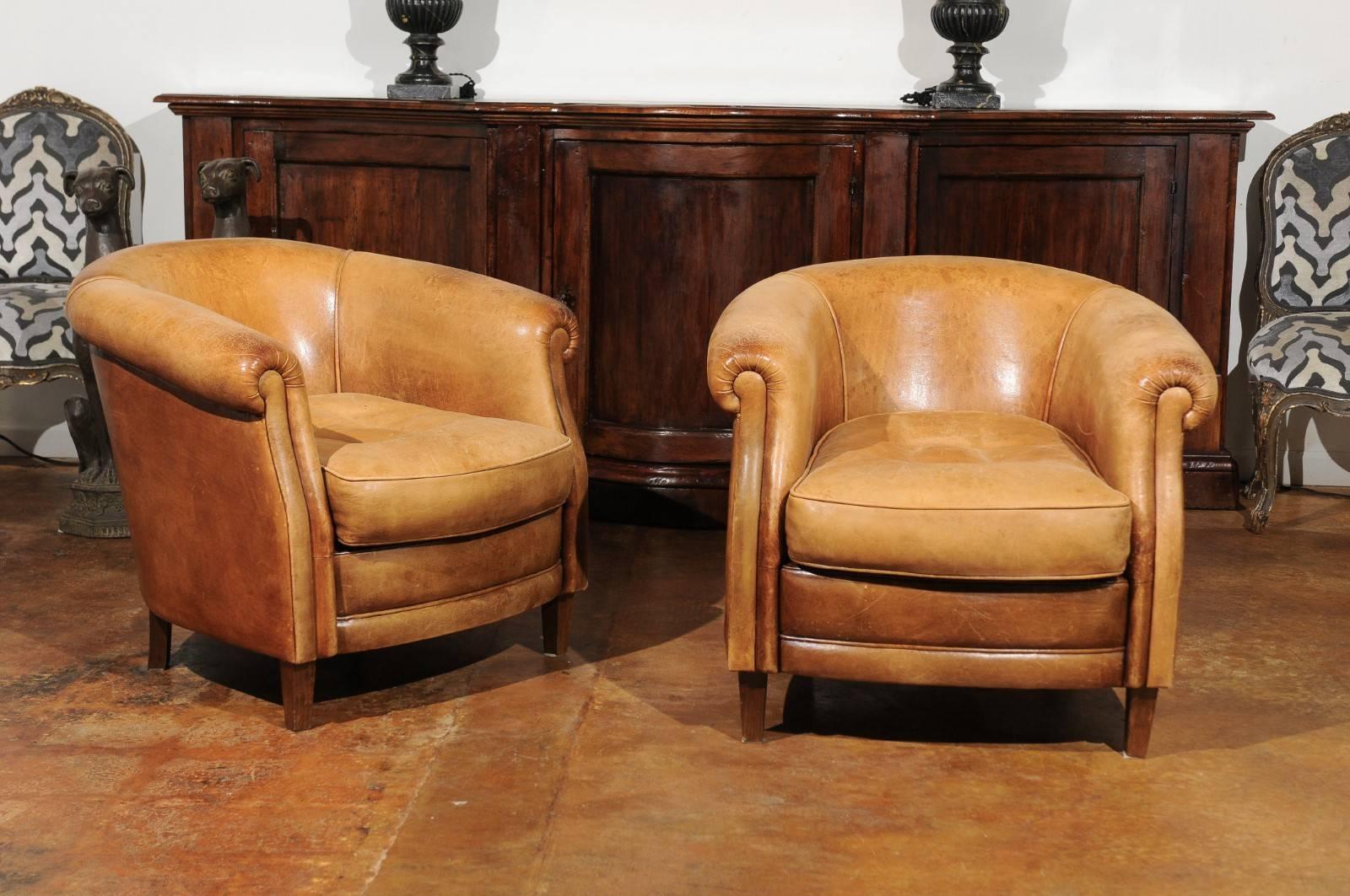 A pair of English caramel club chairs with wraparound backs from the early 20th century. Each of this pair of English leather armchairs features a wraparound back, easily flowing into two large rolled arms. Each seat comprises a comfortable single