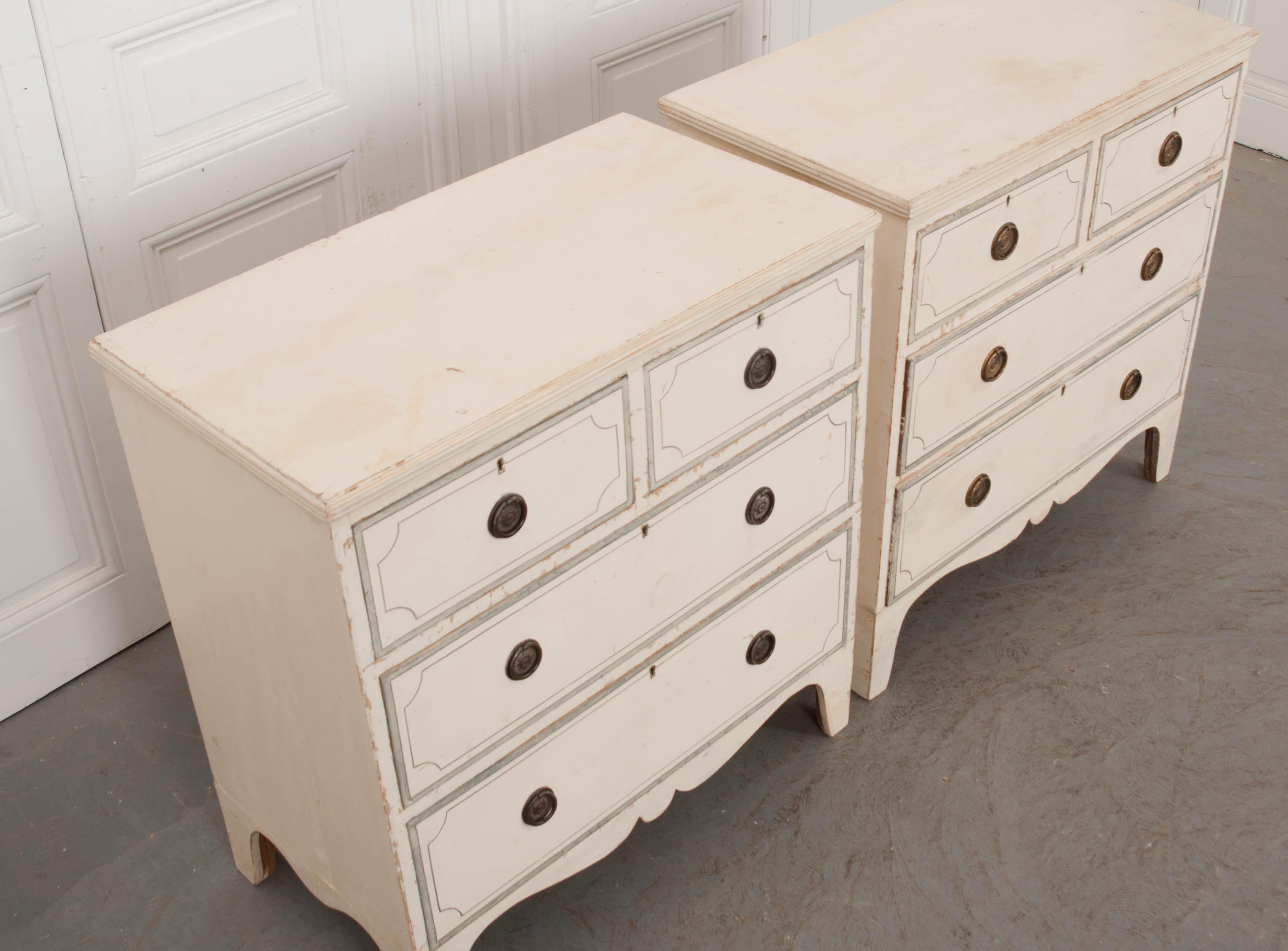 A delightful pair of Edwardian cream-painted chests of drawers, from turn of the 20th century England. Each features two short drawers over two long drawers with hand painted blue-grey accents and round patinated brass pulls. Diminutive in size,