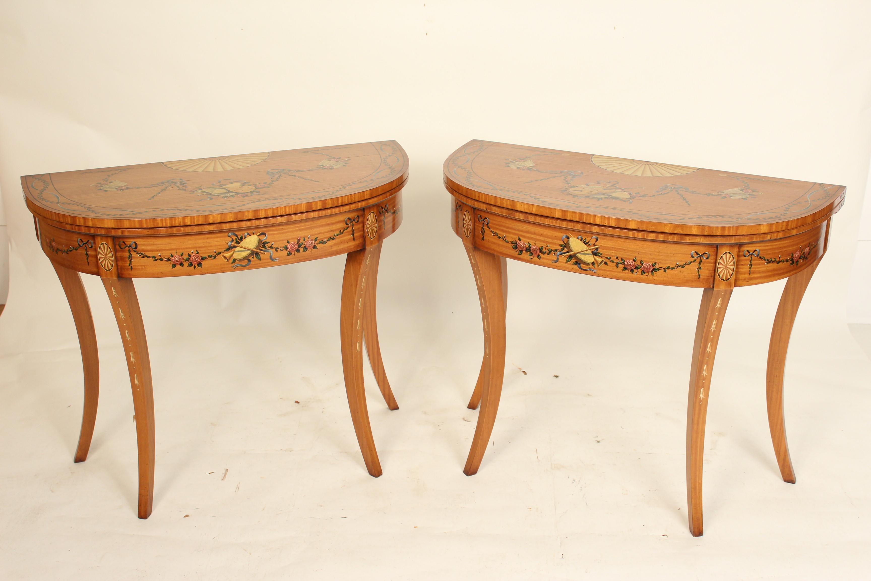 Pair of English Edwardian style painted satinwood, demilune shaped, console games tables, mid-20th century. Paint decorated with floral and musical trophies. Inside games surface is green felt.