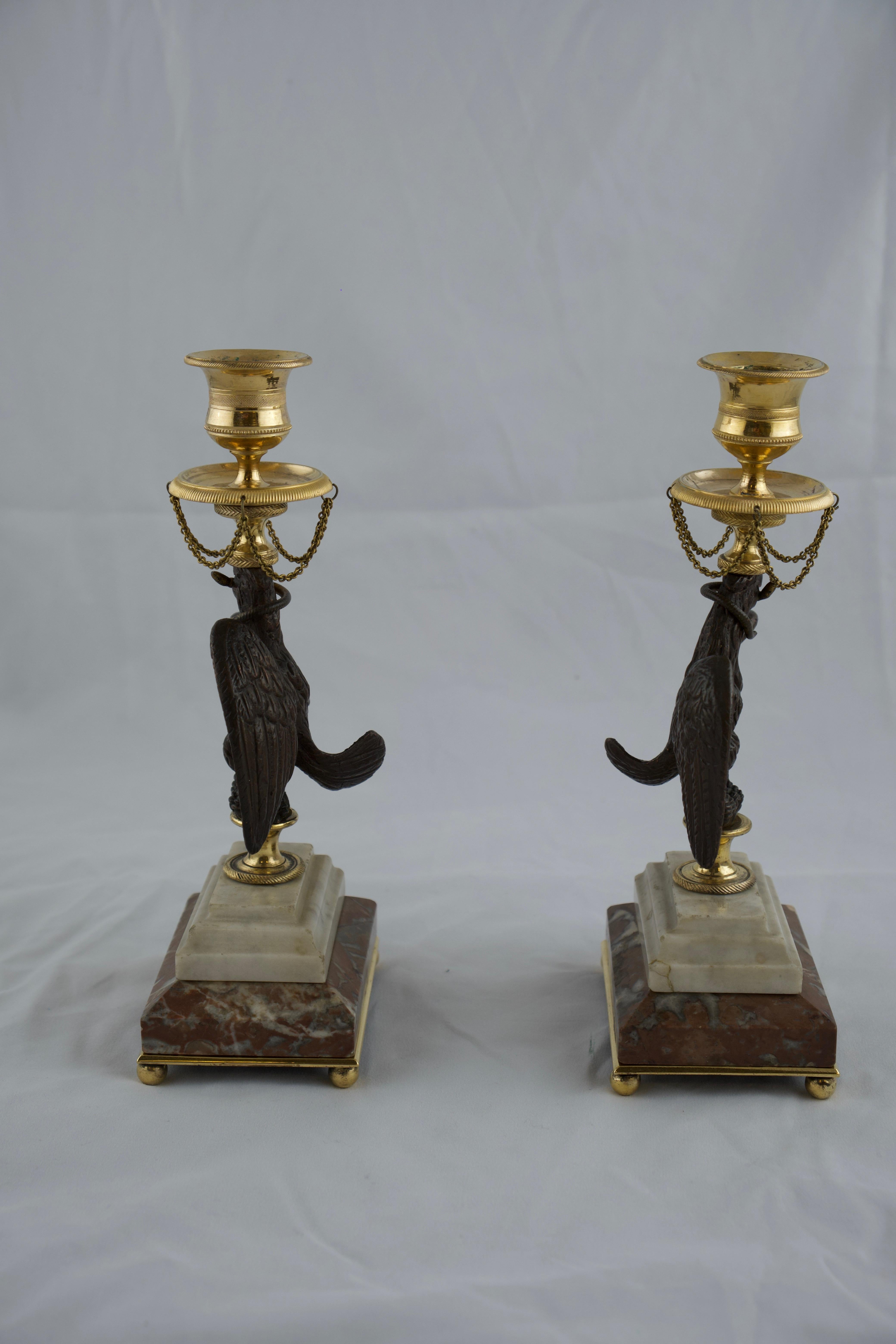 A rare and finely designed Empire candlesticks made in the early 19th c. Standing on a rectangular marble base are cast bronze eagles that holds gilt bronze unshaped candleholders. An interesting and good thing is that the eagles are paired so they