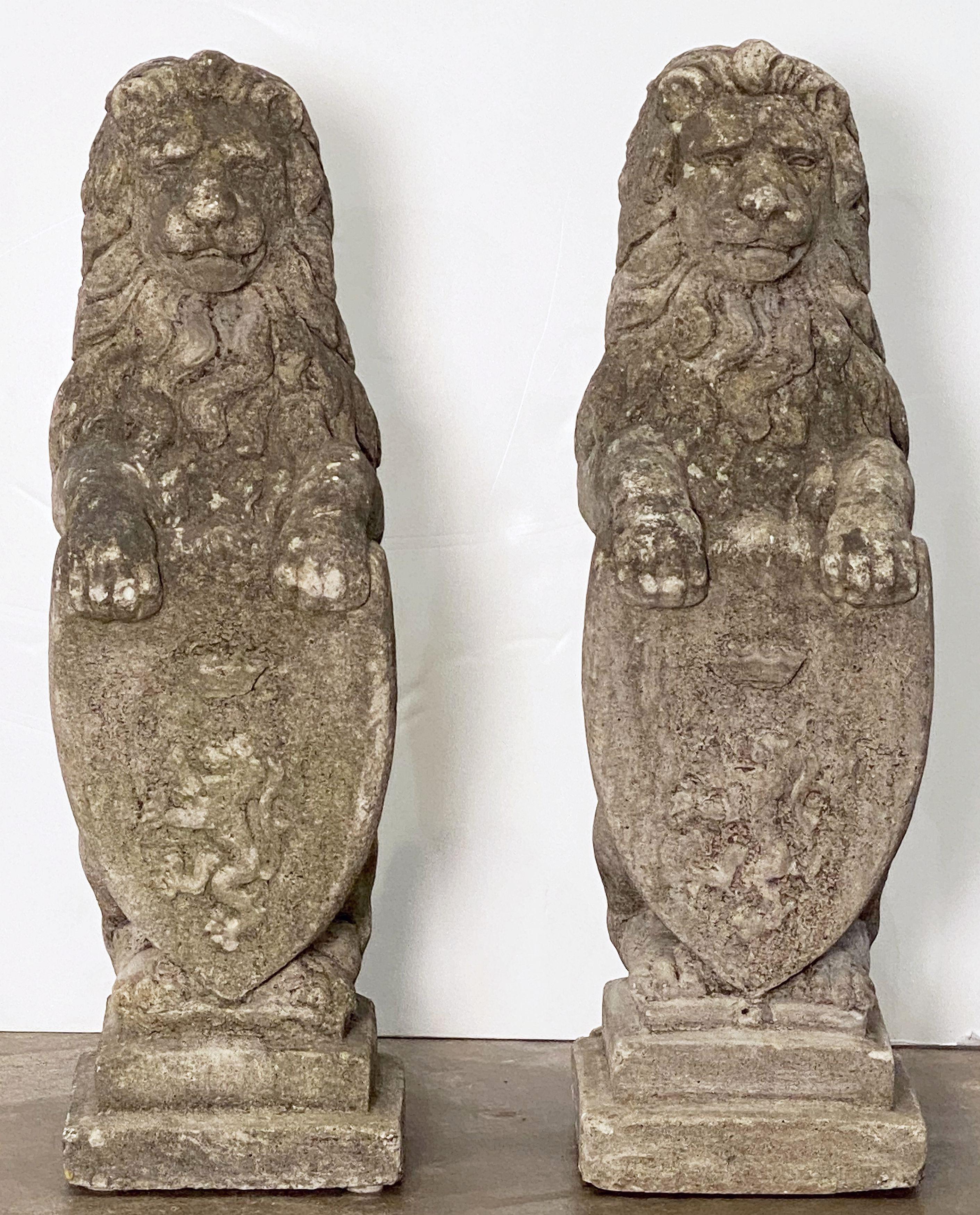 A handsome pair of English standing or sejant-rampant lions on raised graduated square plinths of weathered composition stone - each lion with great detail to head and mane.

Each lion with two raised paws resting on an armorial or heraldic shield