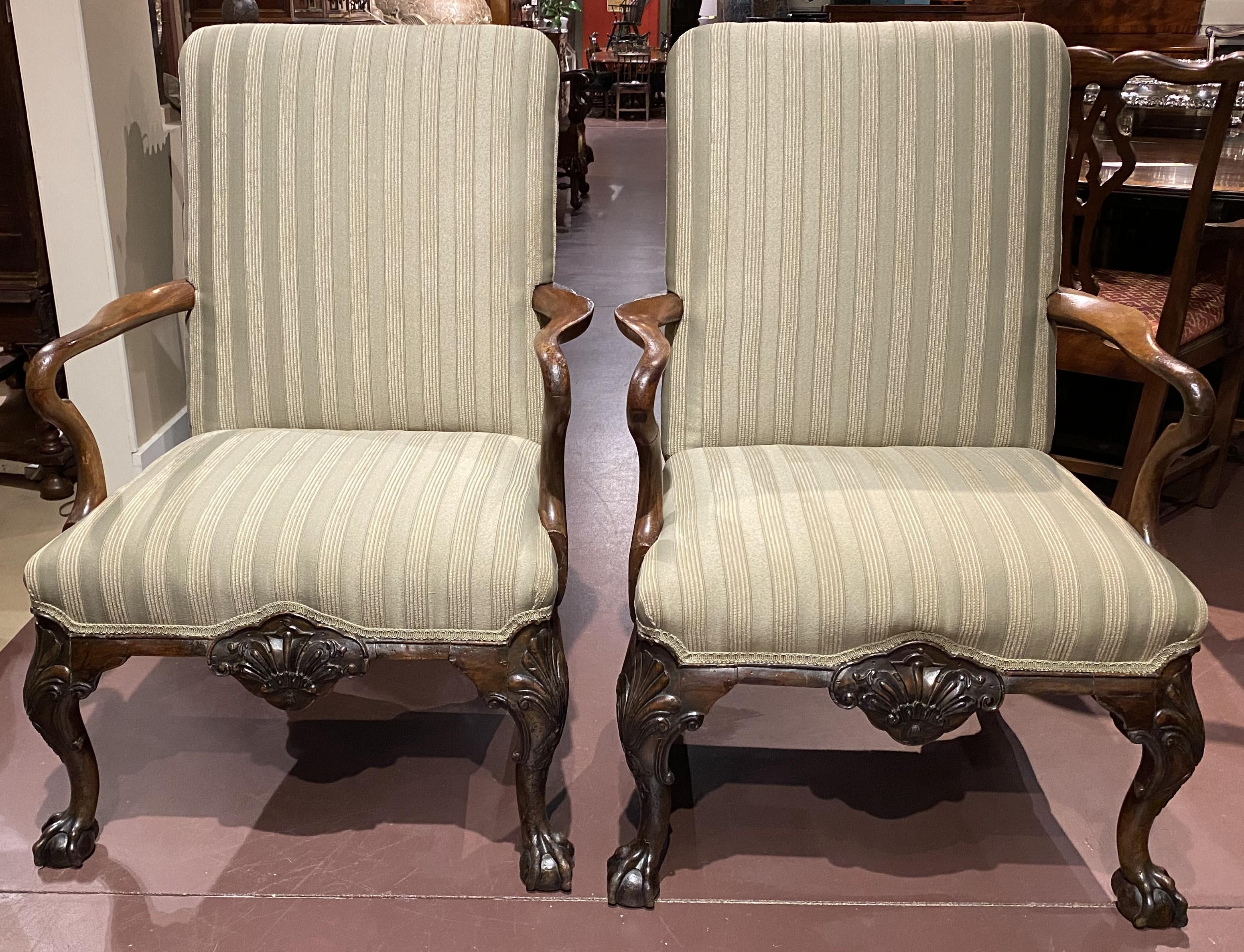 An exceptional pair of English George I style library armchairs in walnut, with nicely carved arms, center carved shell drops, and nicely detailed cabriole legs terminating with ball and claw feet on the front and hoof back feet. The pair dates to