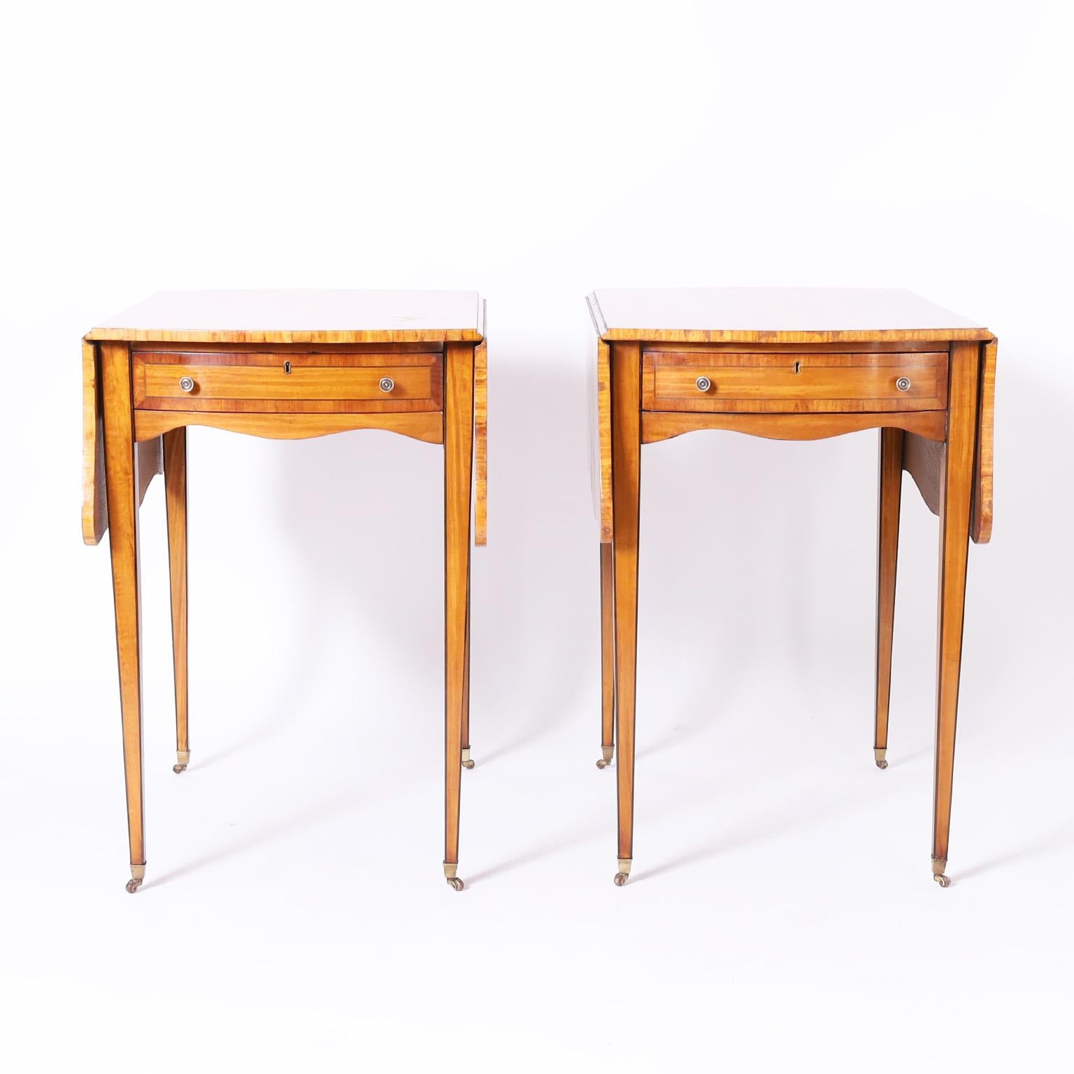 Antique pair of English George III style tables crafted in satinwood with mahogany cross banding in a drop leaf form with one drawer, brass hardware, and long elegant legs on brass casters.

Closed depth: 32