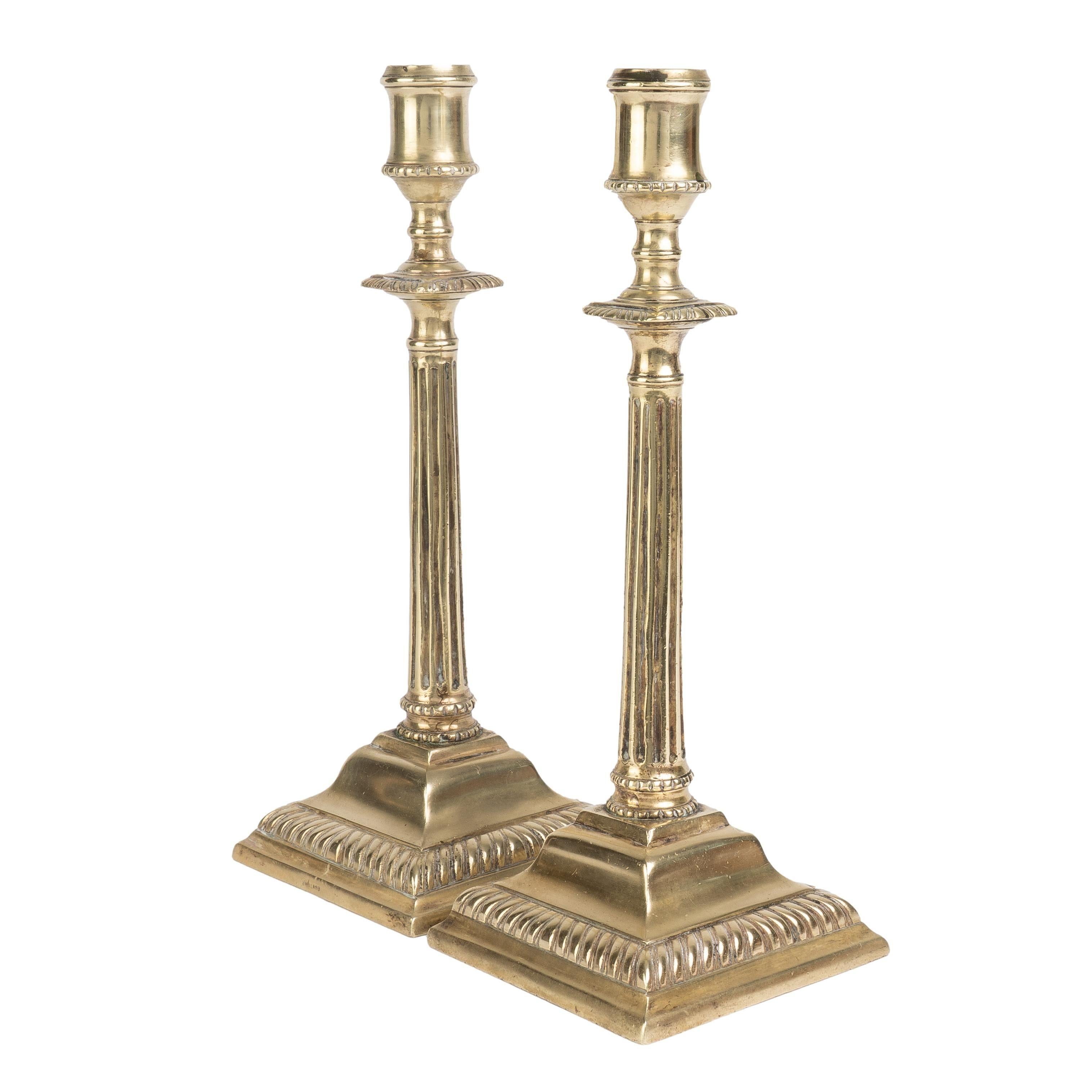 Pair of Georgian cast brass candlesticks with a fluted shaft on square stepped and gadroon edged base with a square gadroon edge drip ring below the candle cup.

Birmingham, England, circa 1790-1800.