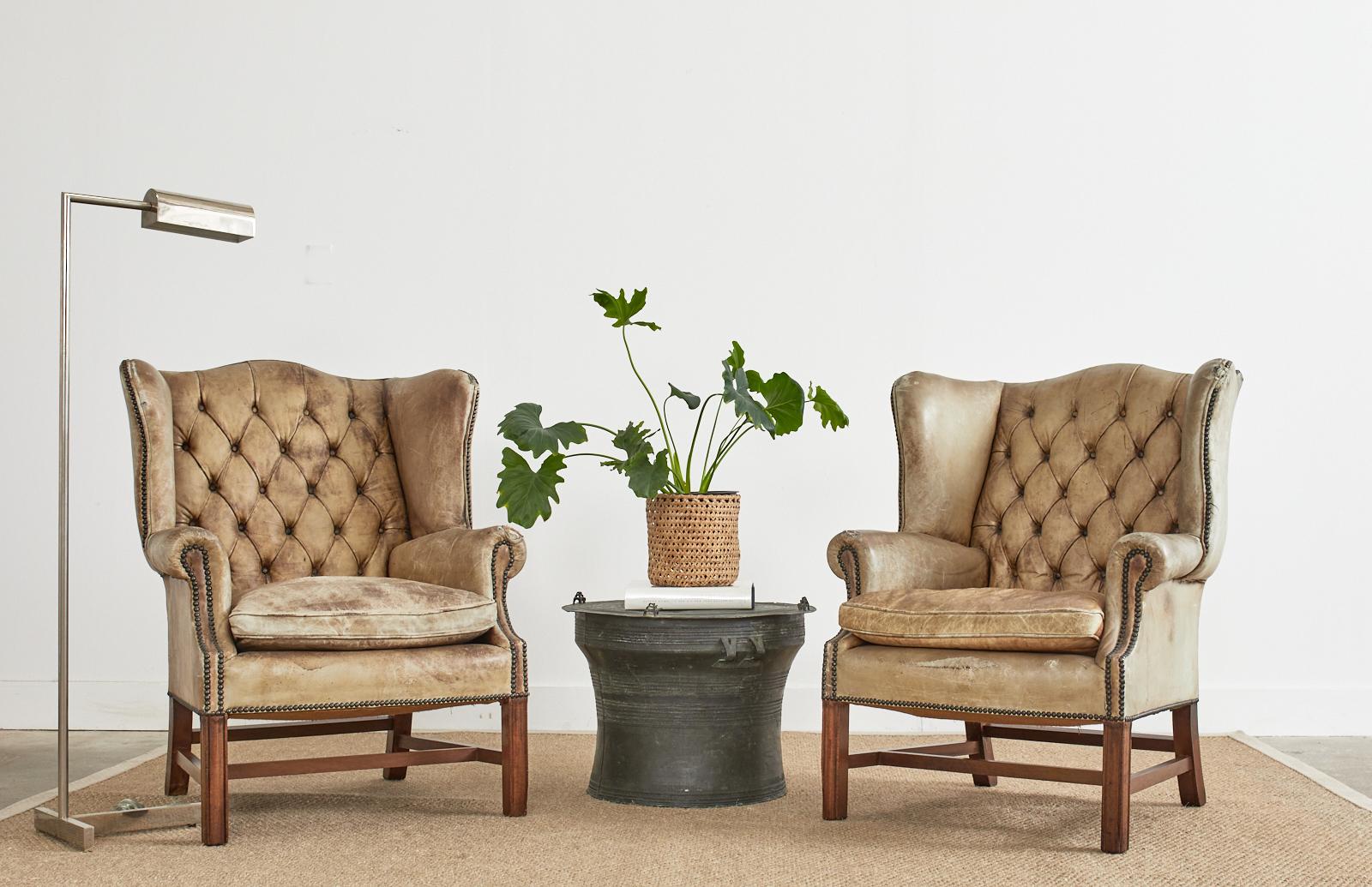 Distressed pair of 19th century English Georgian wingback library chairs. The distinctive pair of armchairs feature a mahogany frame covered with faded cigar leather having brass tack nail head on the border trim. Crafted in the chesterfield style
