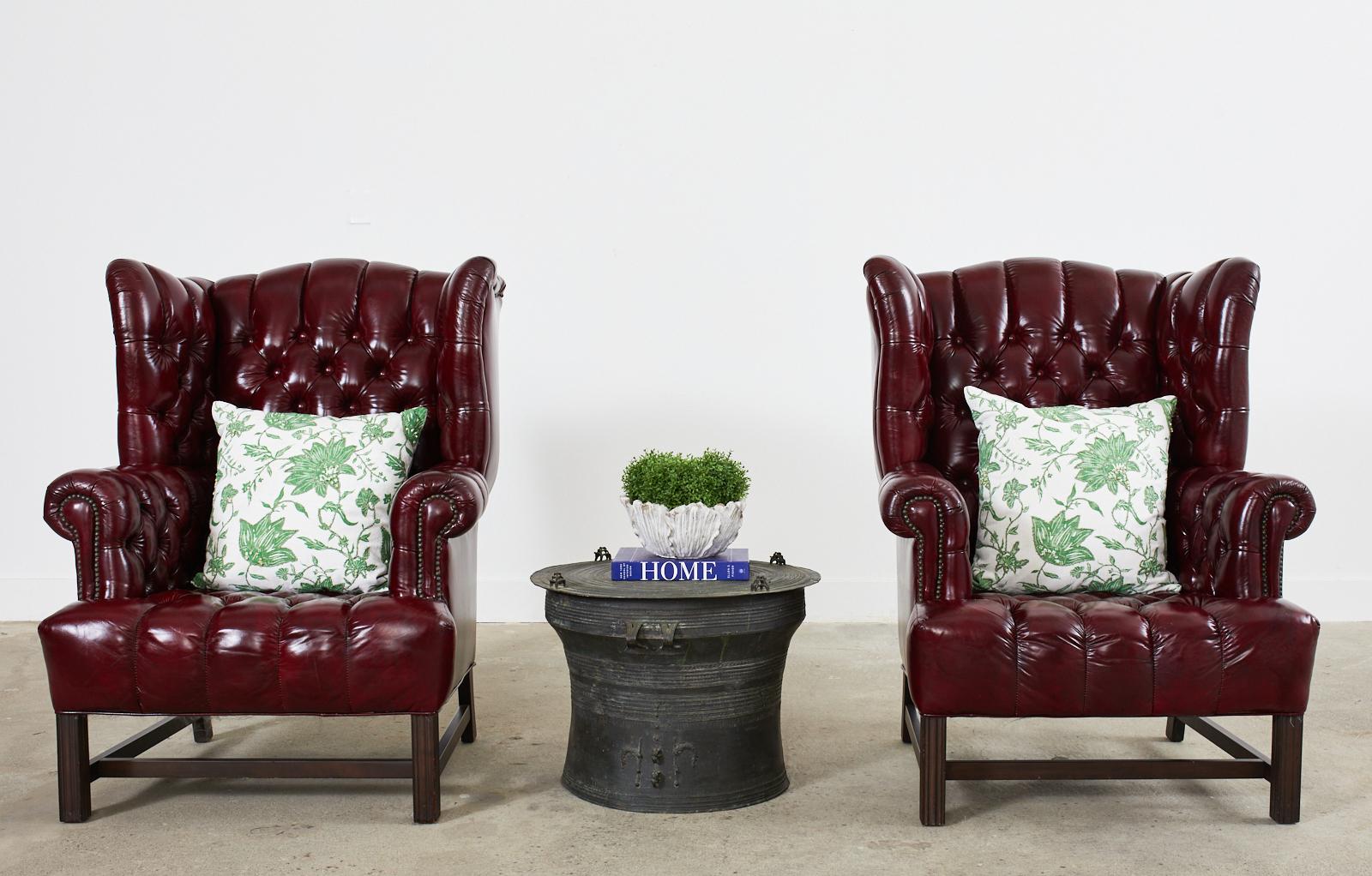 Opulent pair of English George III style tufted wingback armchairs. Made in the chesterfield style featuring a mahogany frame with a generous seating area and large fully developed wings. The English style rolled arms are accented by patinated brass