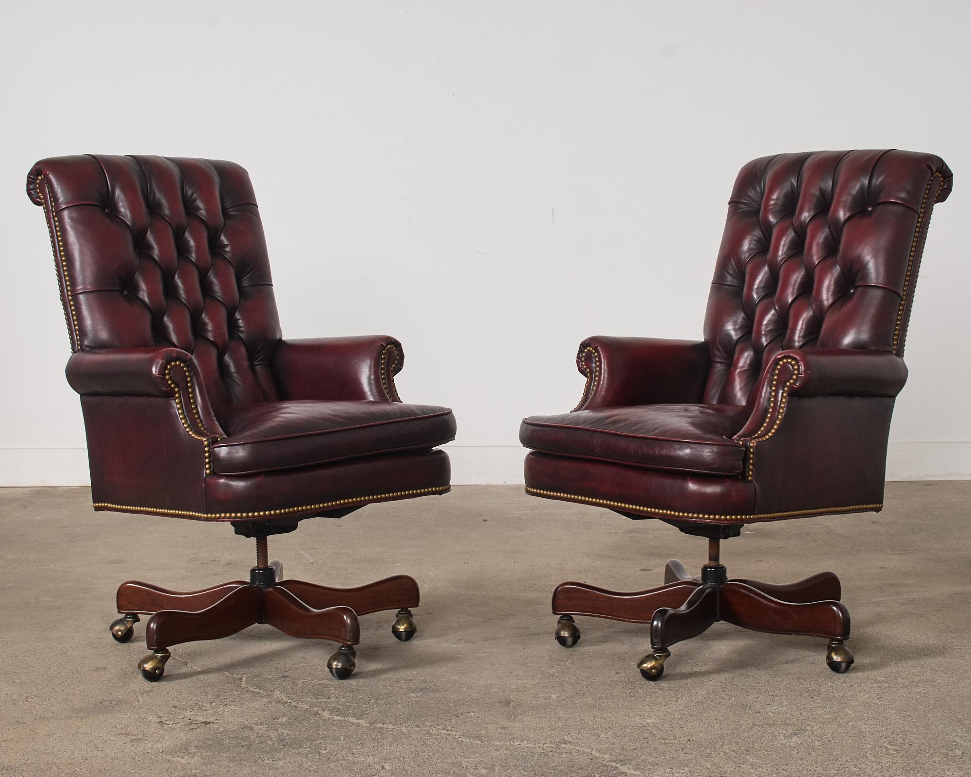 Classic matching pair of Chesterfield cordovan executive office swivel tilt armchairs made in the English Georgian taste. The chairs feature a leather tufted seat with a regency style scrolled back and English rolled arms. The generous seat has a