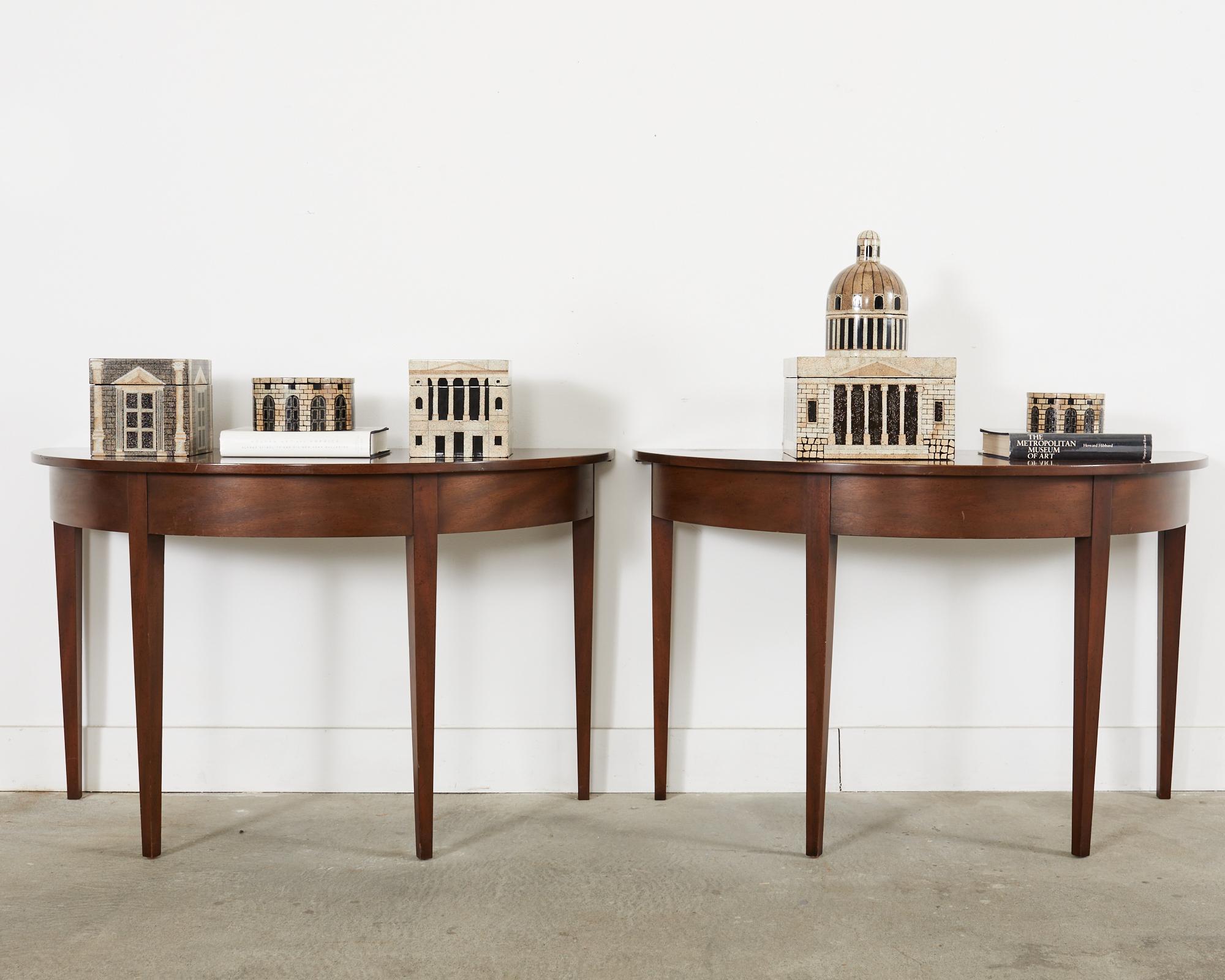 Distinctive pair of mahogany demi-lune console tables hand-crafted by Kittinger. The pair are made with a minimalist aesthetic and free from inlay and decoration as most Georgian period pieces have. The consoles can be used together form a dramatic