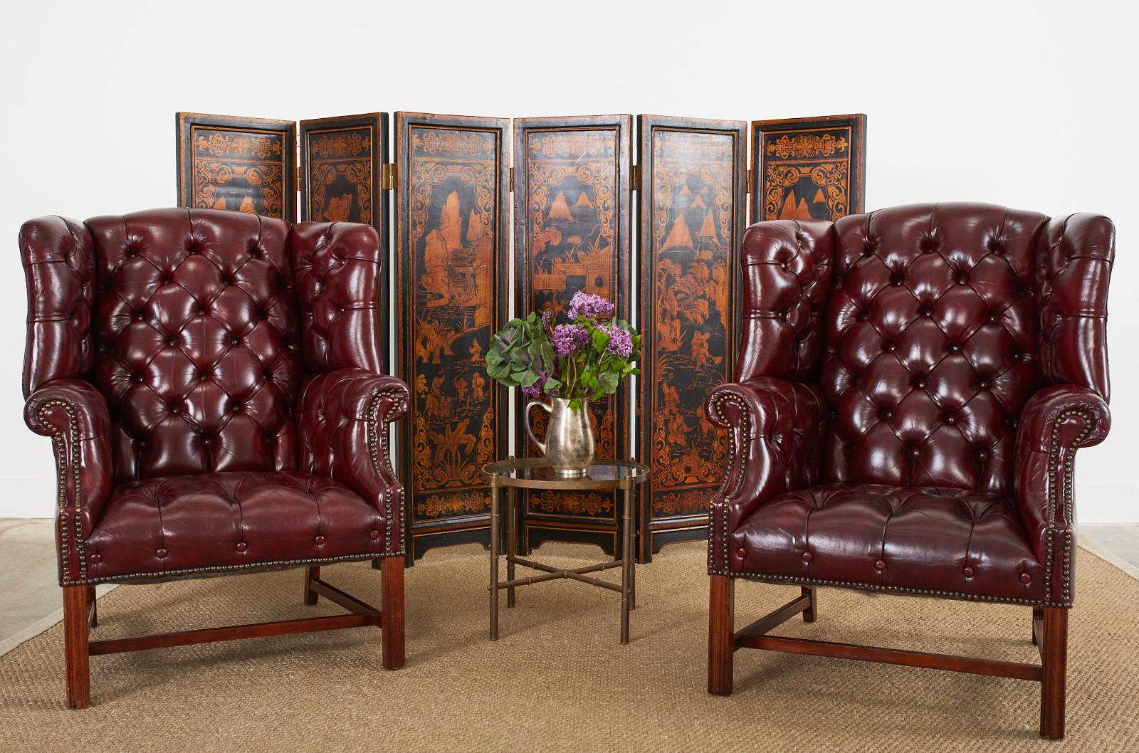 Stately pair of English cordovan or oxblood leather wingback armchairs made in the Georgian style. Crafted from mahogany frames with large, fully developed wings and English rolled arms. The handsome button tufted leather is accented by brass tack