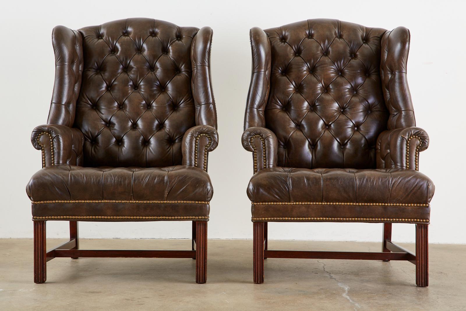 Stately pair of English Georgian style wing back armchairs with matching ottoman by Schafer Brothers. Featuring mahogany frames covered with a marbleized or textured finish on the fine leather. Tufted seat, back, wings, and ottoman with decorative
