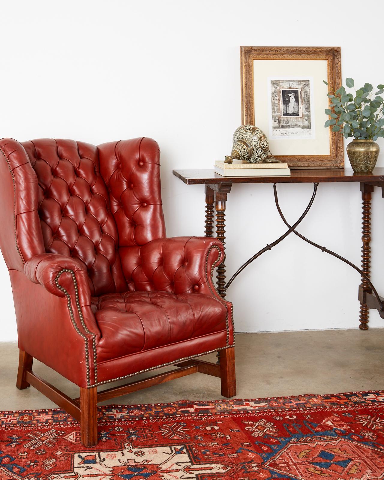 Spectacular pair of midcentury English tufted red leather wingback armchairs made in the Georgian taste. Featuring a generous mahogany frame with a deep seat covered with top grain English leather having a lovely worn patina. The leather is bordered