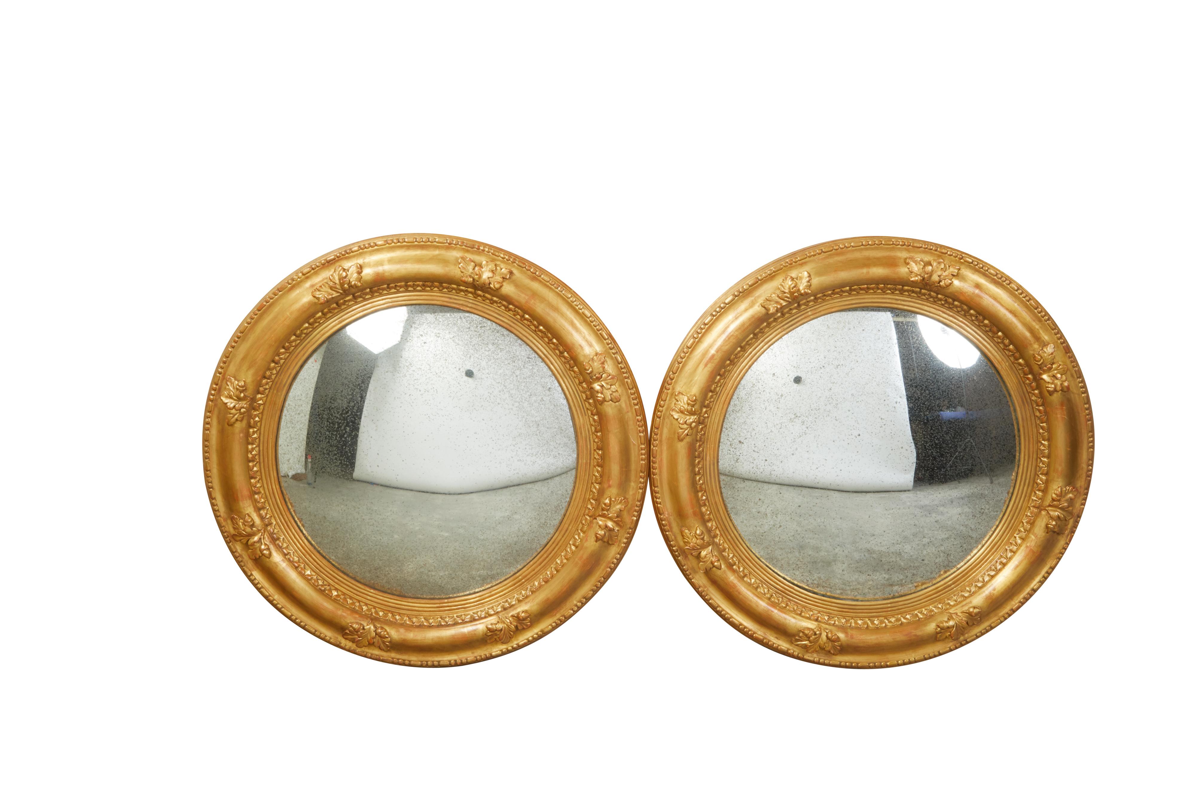 A pair of English giltwood convex mirrors from the mid 20th century, with carved acorns and foliage motifs. Created in England during the first half of the 20th century, each of this pair of giltwood mirrors features a circular frame accented with