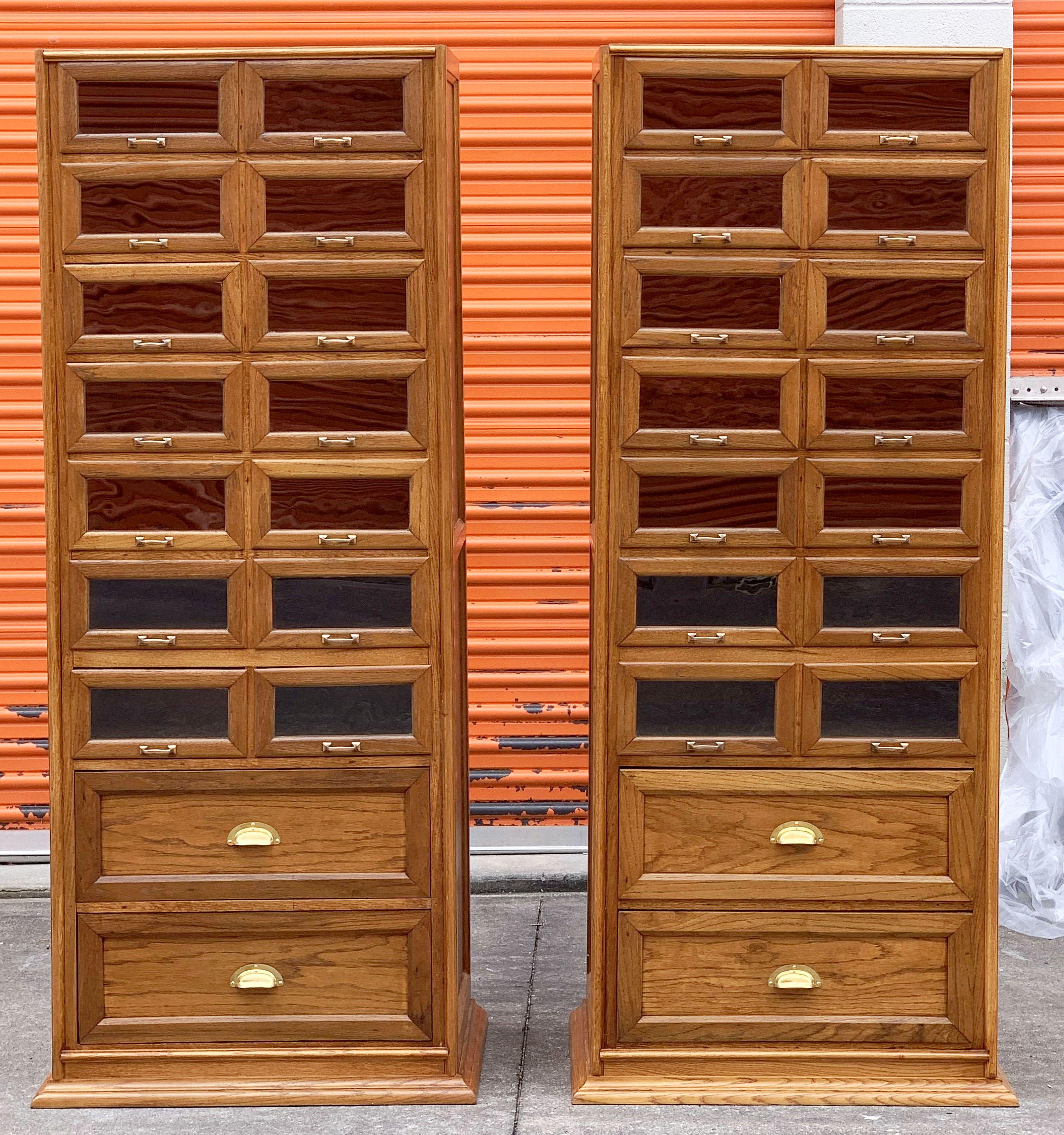 An exceptional pair of large haberdashery or haberdasher's cabinets from England - each featuring:

14 glass fronted drawers over two cupboard drawers, 16 drawers total on each industrial style cabinet.

The fitted drawers with handsome brass