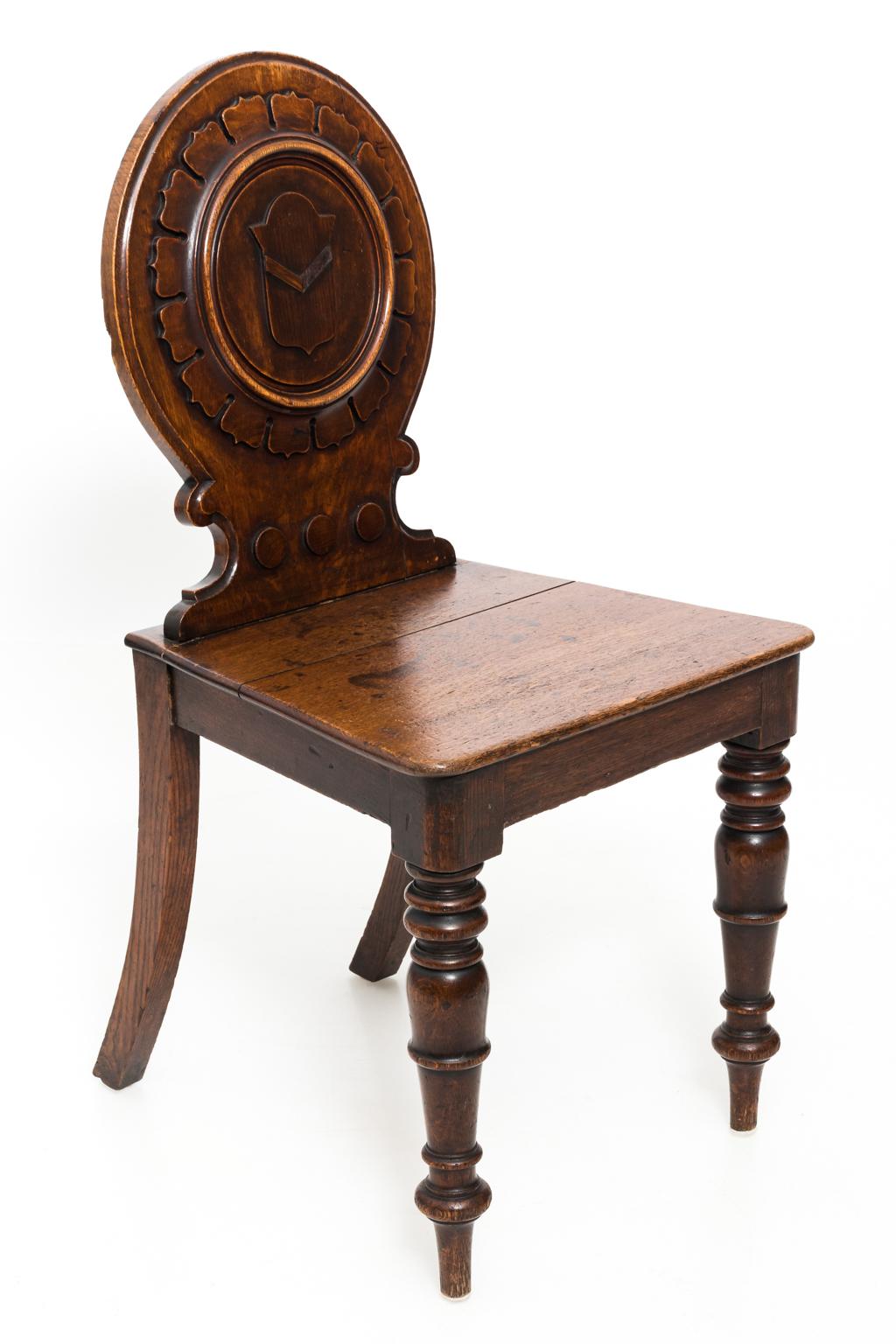 Pair of English oak hall side chairs with center shield crest, circa 1880-1890. The chairs also feature ring turned legs. Please note of wear consistent with age on the seat including worn edges and gapping in the wood.
 
