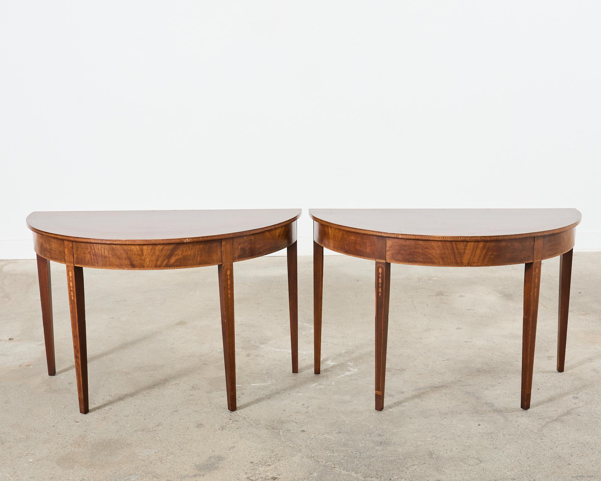 Late 19th century matched pair of English demilune console tables made in the Hepplewhite or federal style. Crafted from mahogany with rich, radiant veneers and delicate inlay. Originally ends of a grand banquet table. The ends fit together to form