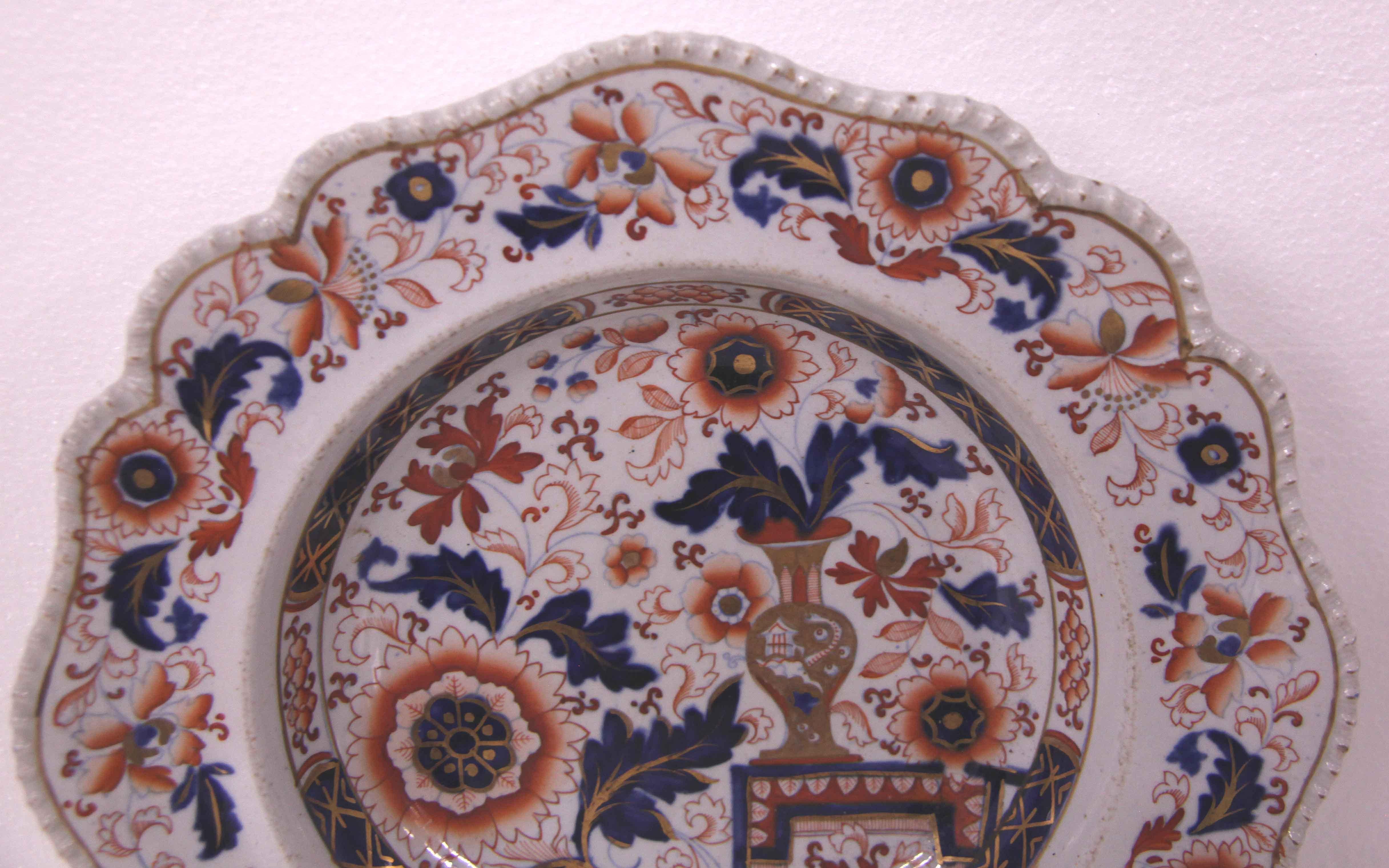 Pair of English ironstone soup plates, with a scalloped and beaded rim, the border has a repeating pattern of stylized flowers and foliate, the interior of the plate features a variety of flowers and foliate and a gilded vase sitting on a plinth. On