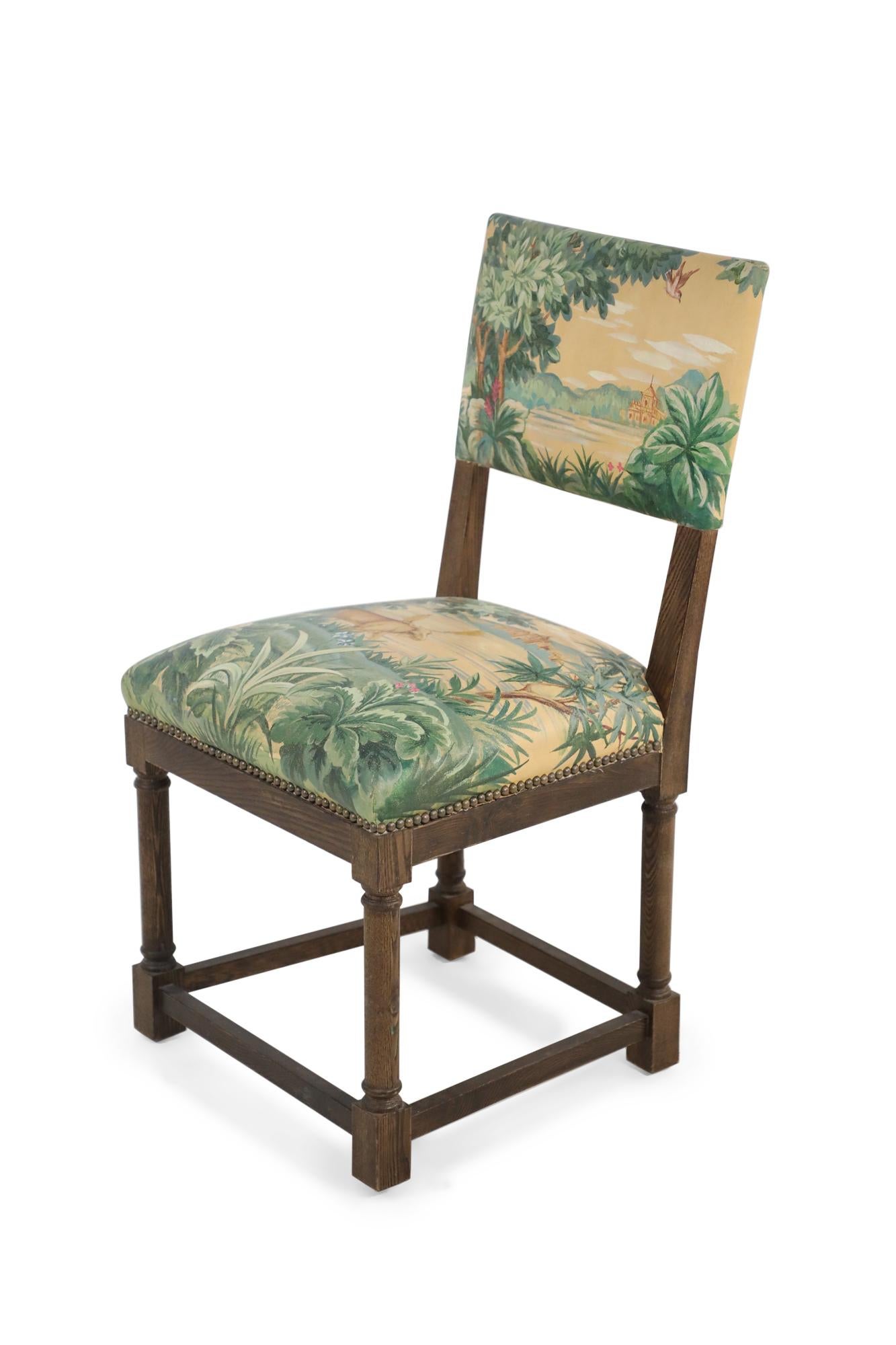 Pair of English Jacobean-style side chairs with walnut frames and hand-painted faux-tapestry upholstery featuring a pastoral scene in greens and yellows.