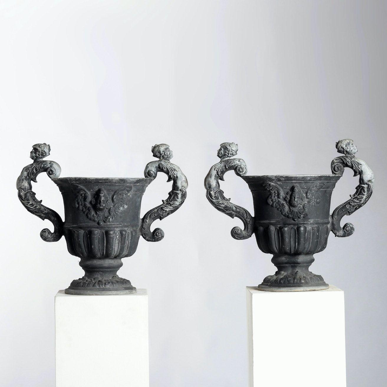Exceptional pair of English lead urns. Round, with a gadrooned waist, the sculpted lead depicts a winged cherub with scrolling handles terminating in female nudes that resemble mermaids. Circa 1960.
