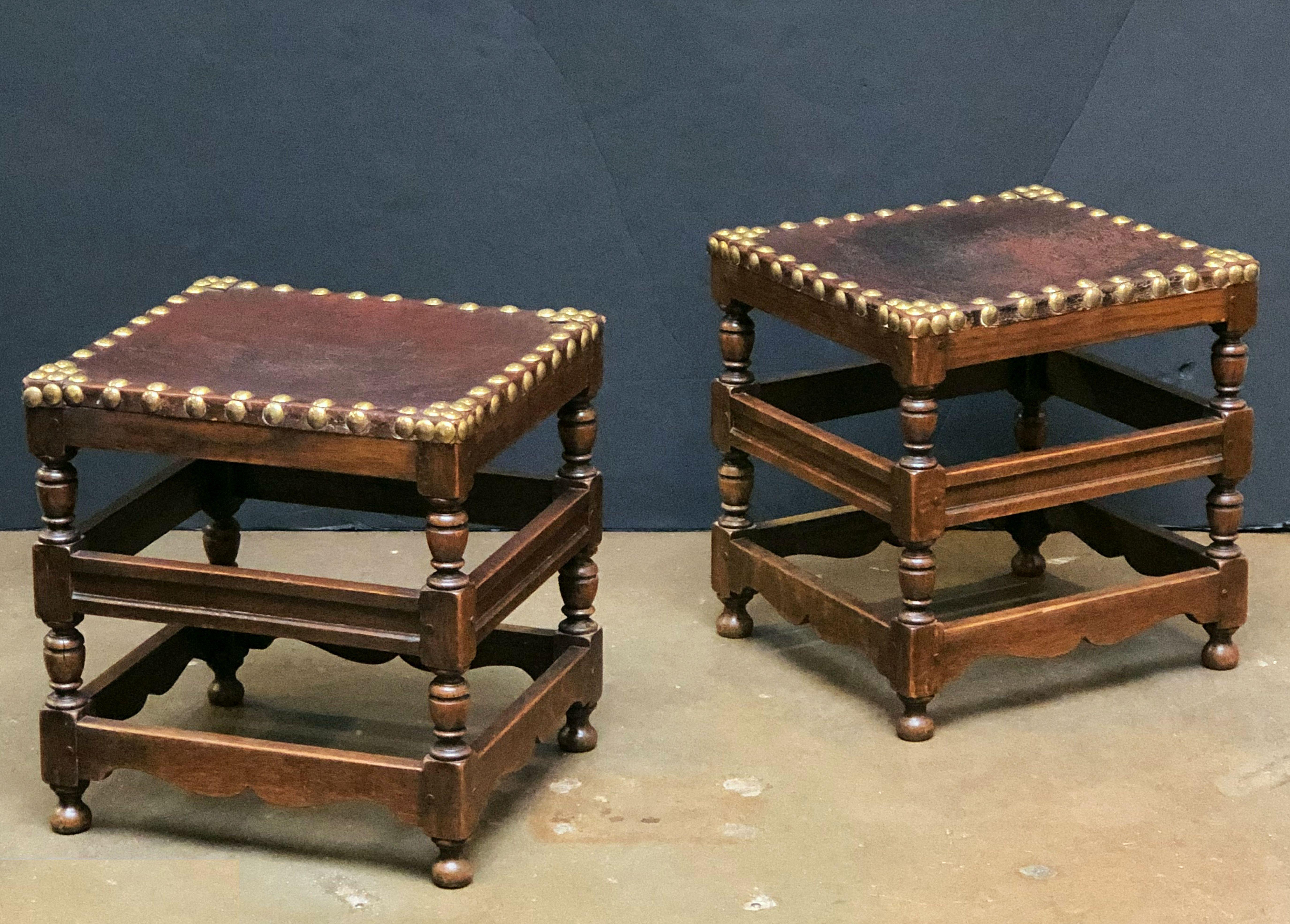 A fine pair of English foot stools from the 19th century, each stool featuring a rectangular leather top with brass nail-head trim over a four-legged stretcher frame of turned oak.

Stool dimensions are:
Height 18 3/4 inches x width 18 1/4 inches