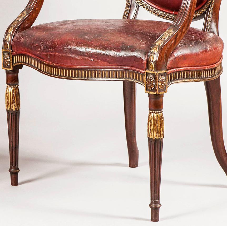 A fine pair of armchairs in the neoclassical in the manner of Robert Adam

Constructed in mahogany with hand-painted gilt accents and red leather, each with oval backs enclosed with interlocking dart and braid carved design, with outswept arms