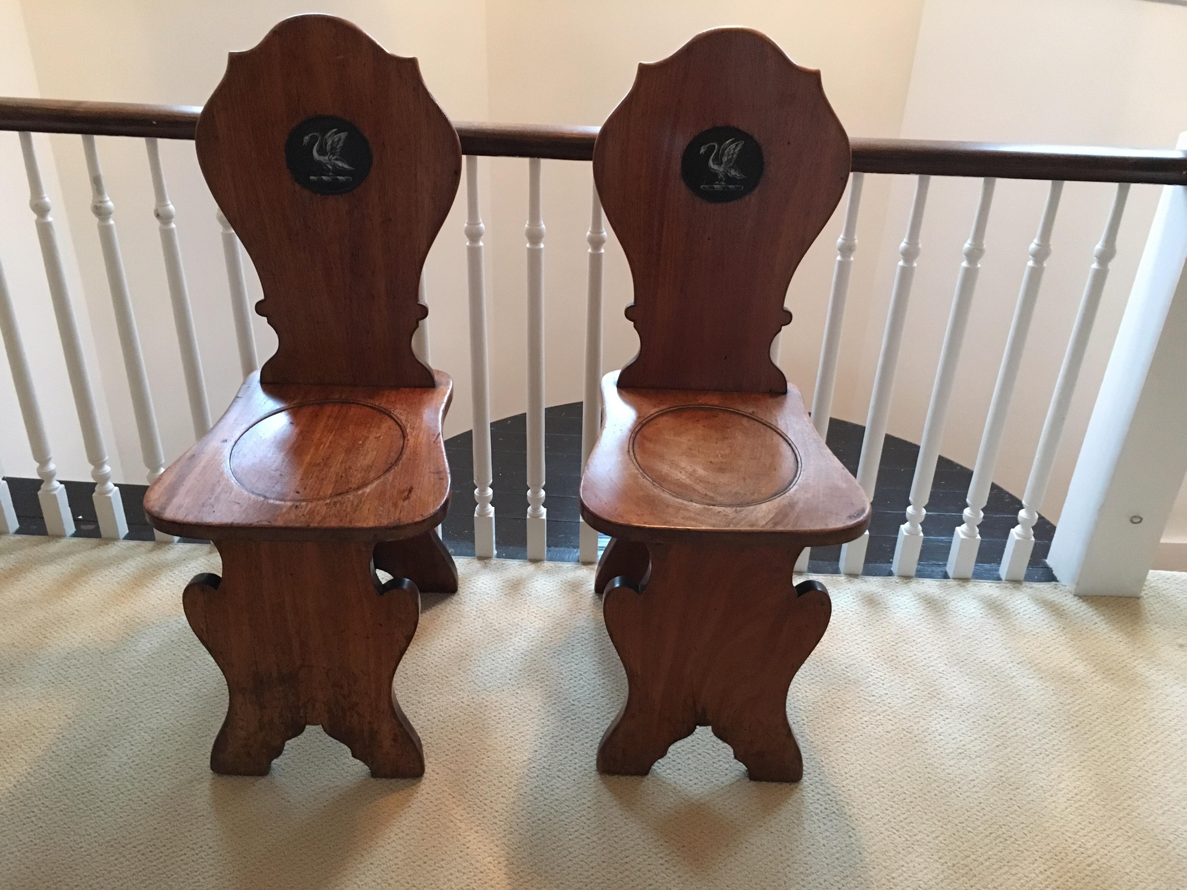 A pair of English mahogany hall chairs from the second half of the 19th century, with hand-painted heraldic swans. Featuring a cartouche back, center medallion adorned with a hand-painted heraldic swan. Seat is slightly recessed in its center.
    