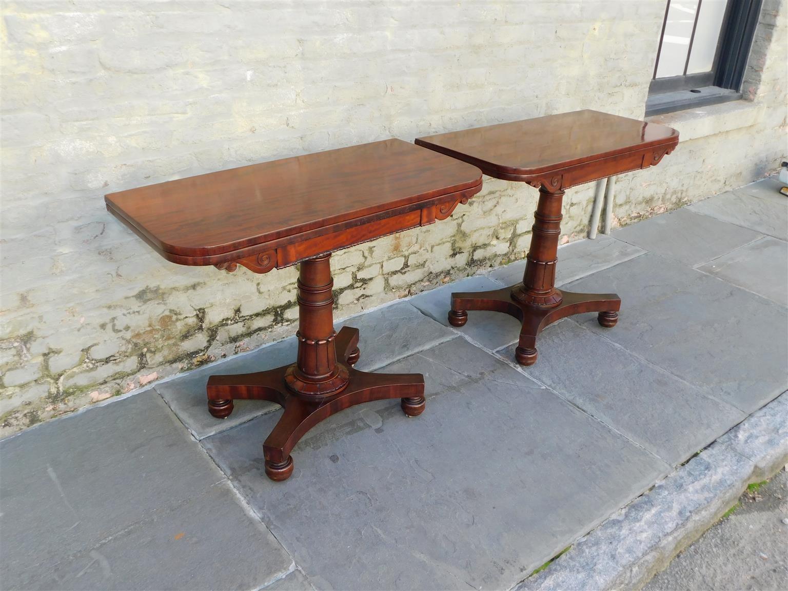 Pair of English mahogany foliage pedestal hinged game tables with flanking scrolled corners, gadrooned skirts, baize card playing surfaces, open interiors for storage, and resting bun feet with the original brass casters, Early 19th century.
Pair of