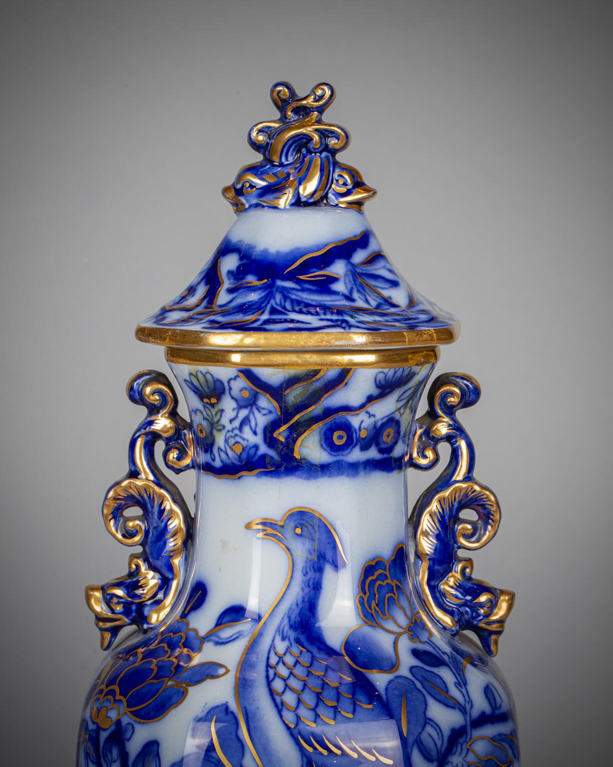 Decorated in various tones of blue on a gray ground with stylized birds and flowers with gilt highlights, with dolphin handles and twin dolphin finials.