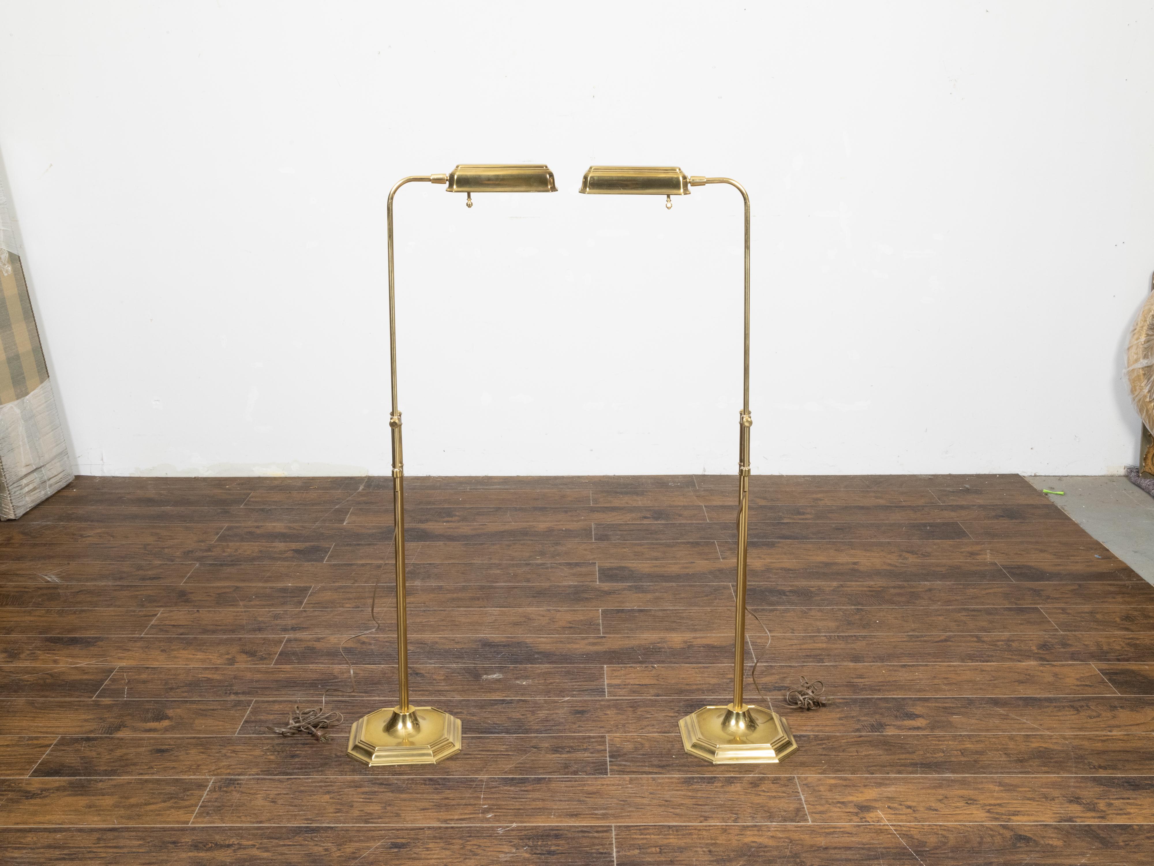 A pair of vintage English brass floor lamps from the mid 20th century, with adjustable heights, wired for the USA. Created in England during the Midcentury period, each of this pair of floor lamps have been professionally rewired for the USA and are
