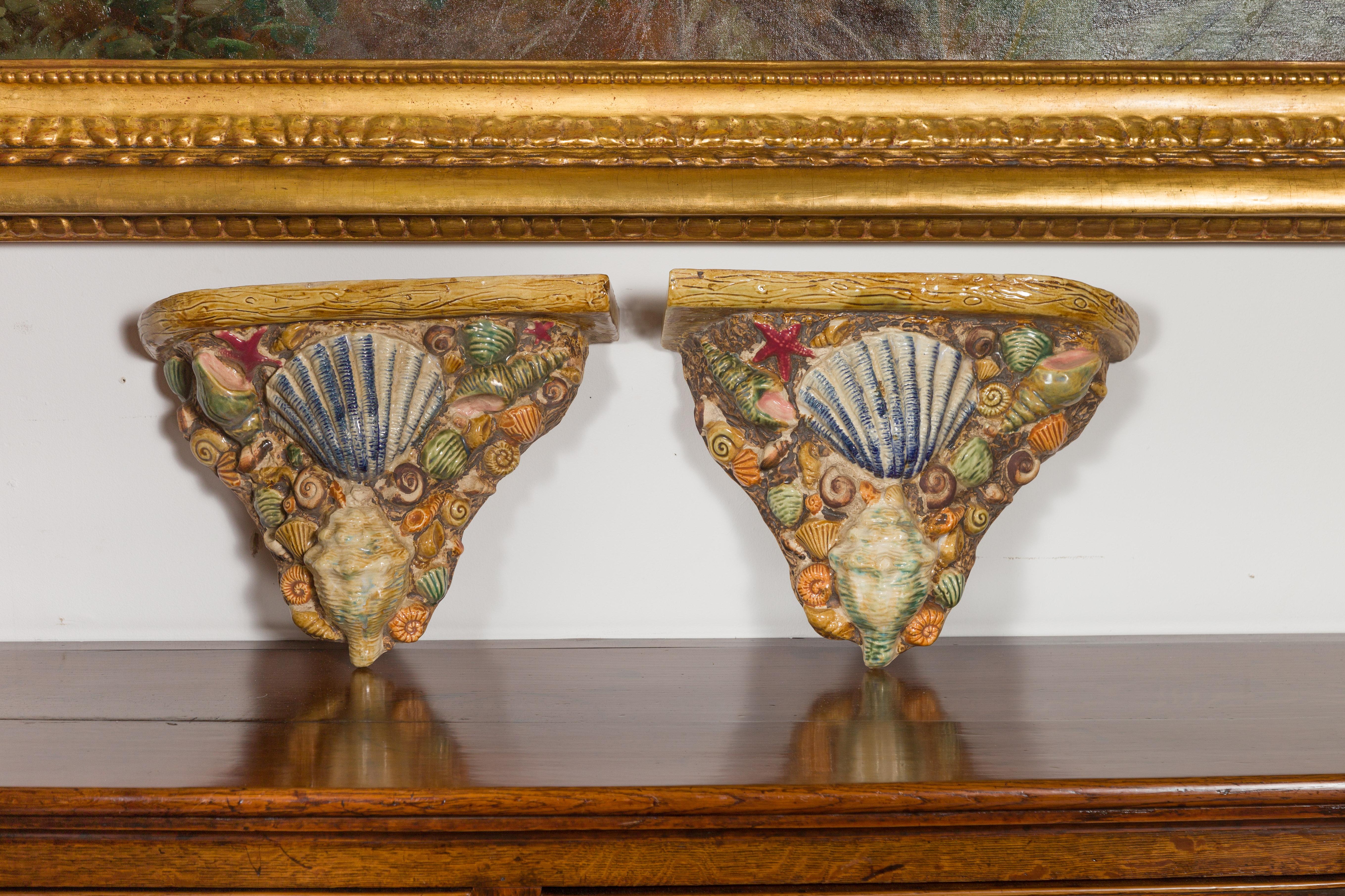 A pair of English majolica brackets from the mid-20th century, with seashell decor. Created in England during the midcentury period, each of this pair of majolica brackets attracts our attention with its colorful depiction of seashells, topped with