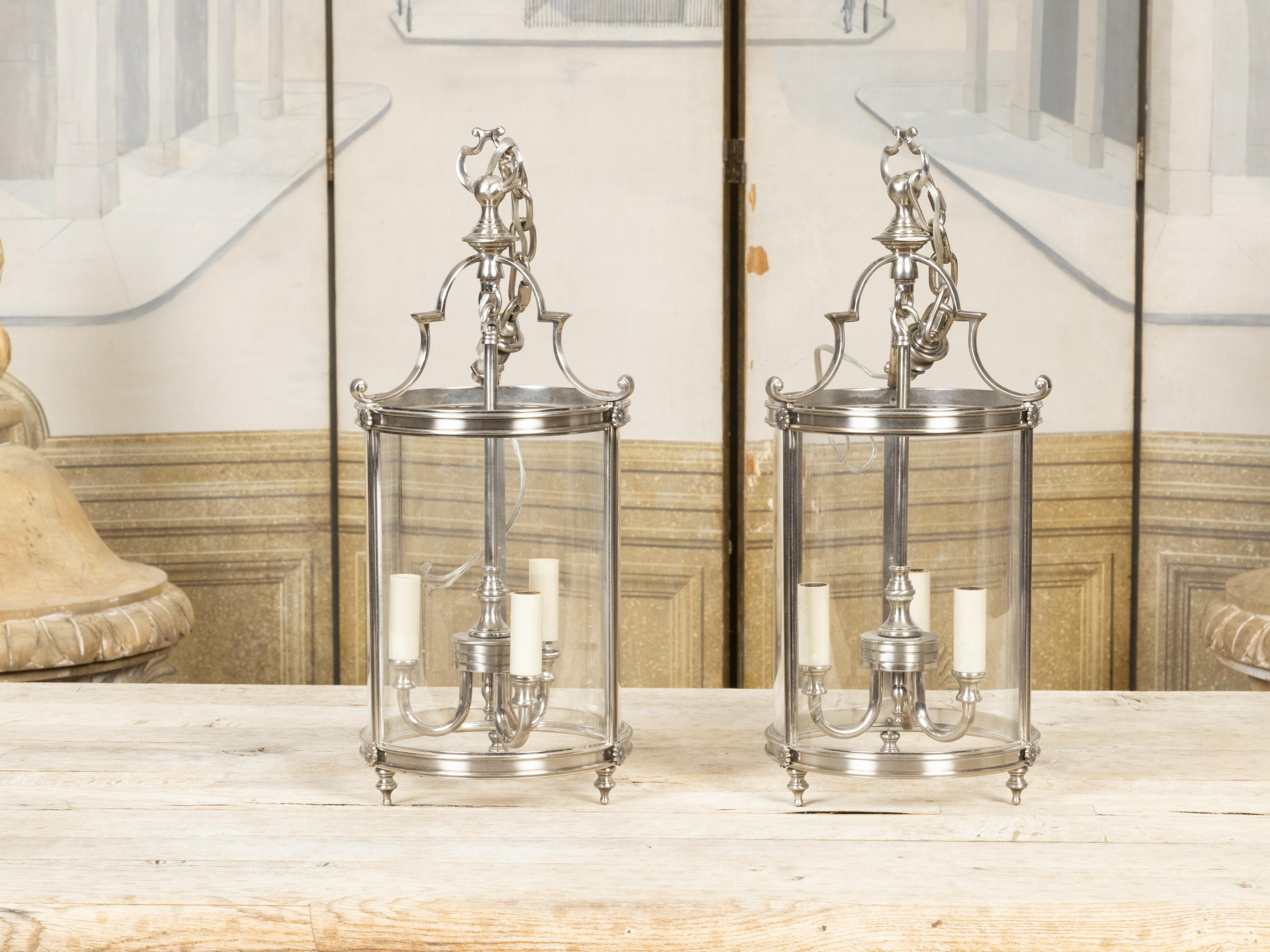 A pair of vintage English metal lanterns from the mid 20th century, with nickel finish, three lights and glass body. Created in England during the third quarter of the 20th century, this pair of hall lanterns attracts our attention with their lovely